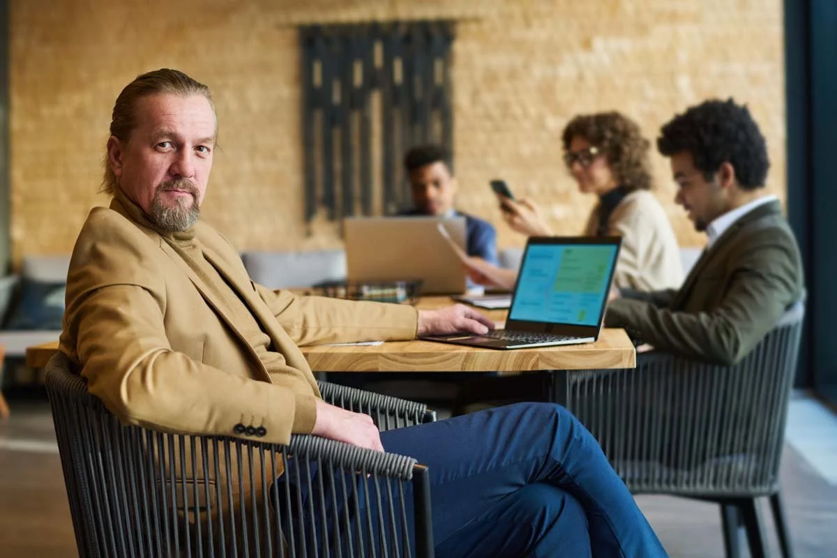 Foto eines Mannes der stolz in einem Stuhl sitzt und über seine Schulter in die Kamera schaut