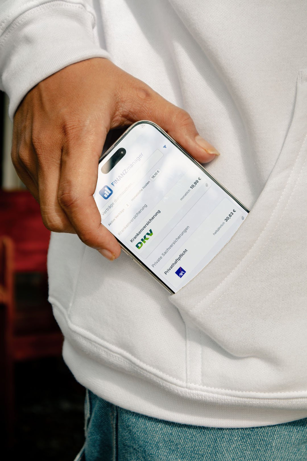 Detailaufnahme einer Hand die ein iPhone in die Tasche steckt. Auf dem iPhone erkennt man die Oberfläche der Finanzmanager App