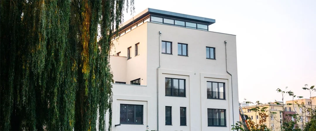 Foto eines modernen Hauses mit mehreren Etagen. Im Vordergrund ein Baum