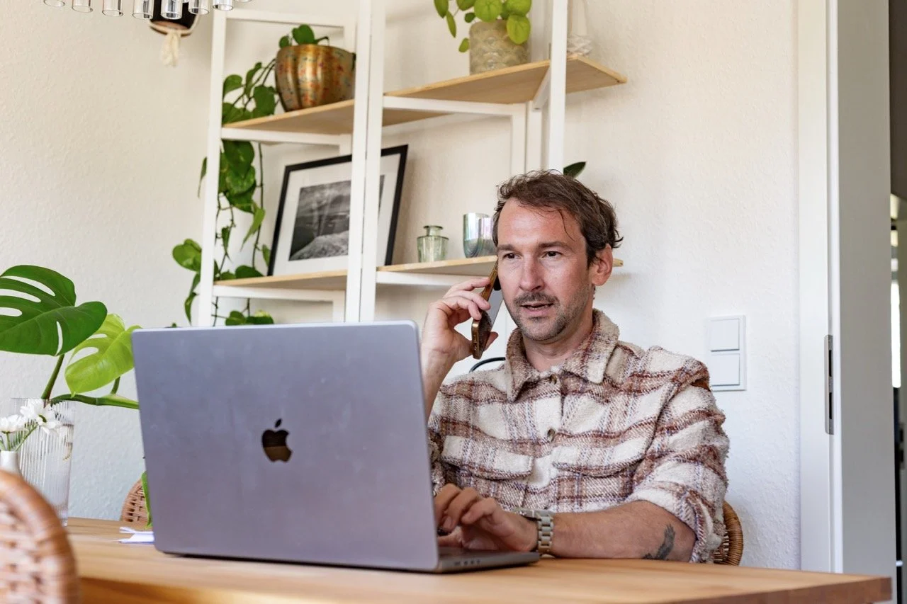 Thomas Ploch am Macbook sitzend und telefonierend während er Gesundheitsfragen checkt
