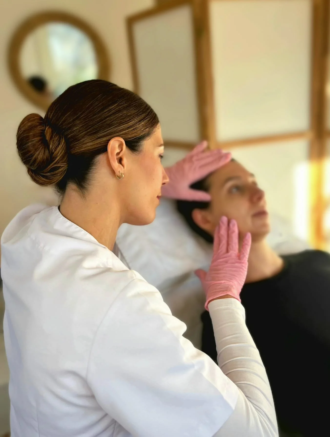 Eine Ärztin in einer Praxis für ästhetische Medizin bei der Untersuchung, während sie den Kopf der Patientin mit einer Hand stützt und die andere Hand auf den Kopf legt.