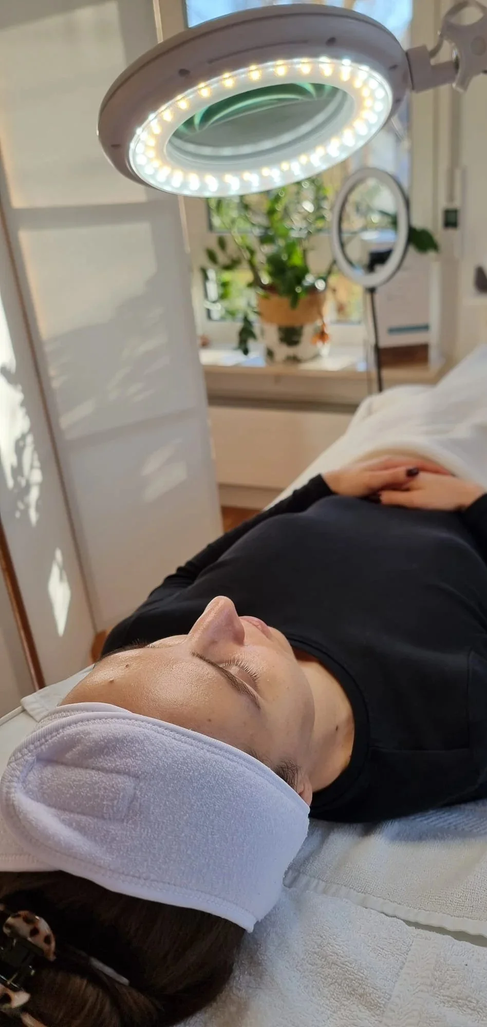 Frau liegt entspannt auf einer Behandlungsliege unter einer Lichtquelle, im Rahmen einer medizinisch ästhetischen Behandlung.