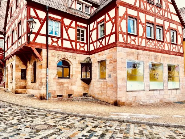 Ein Fachwerkhaus mit zwei Stockwerken und Geschäftsschildern, darunter eine Praxis für ästhetische Medizin auf einer gepflasterten Straße in Lauf an der Pegnitz im Nürnberger Land.