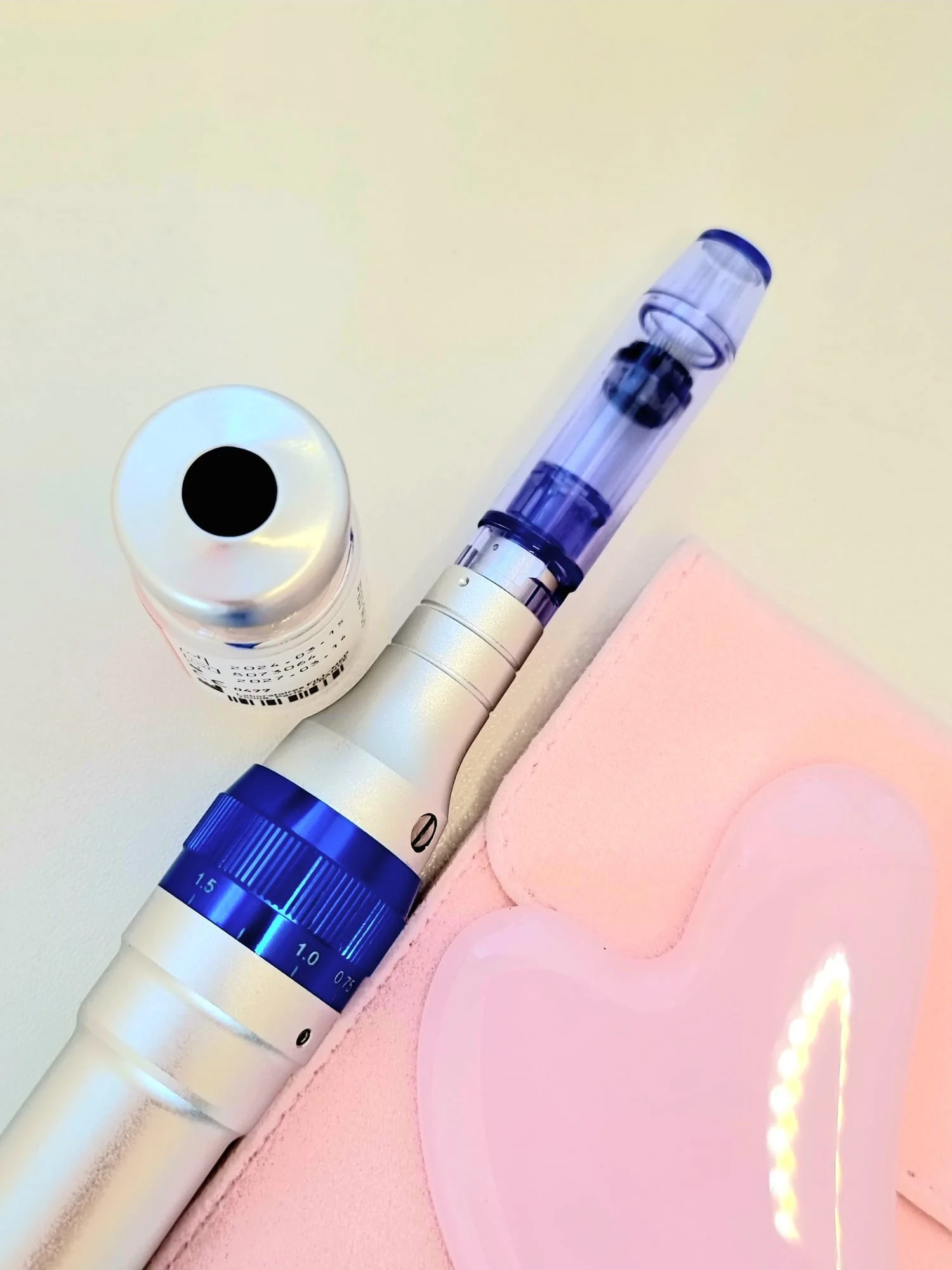 Pen für Microneedling-Behandlung und Injektionsampulle auf rosa Hintergrund.