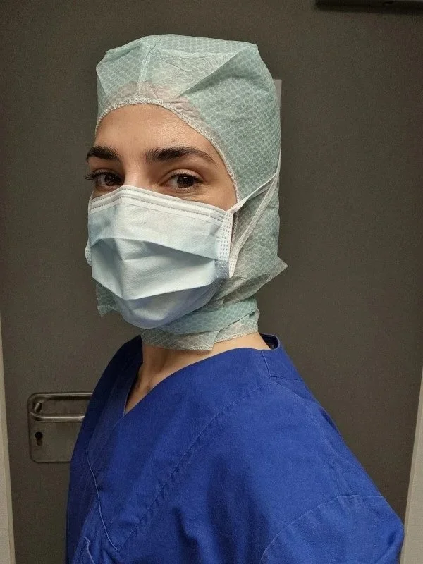 Medizinisches Personal trägt Schutzkleidung, OP-Maske, Haube und blauer Arztkittel.