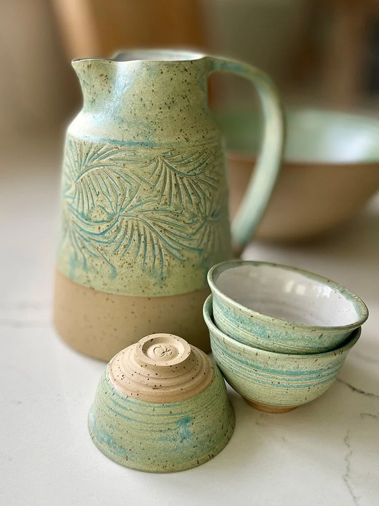 Set of ceramic tableware including a tall pitcher, three small bowls, and a small upside-down bowl, all with earthy tones and decorative patterns.