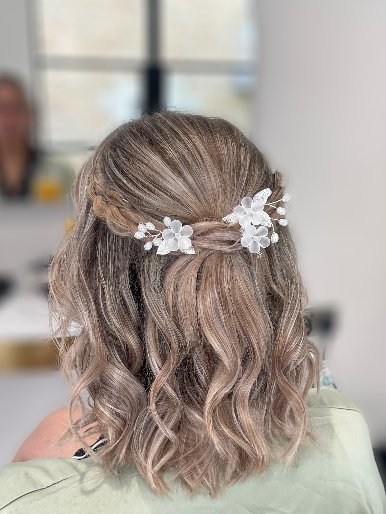 Back view of a woman with wavy, blonde hair styled with a floral hair accessory featuring white flowers and pearls.
