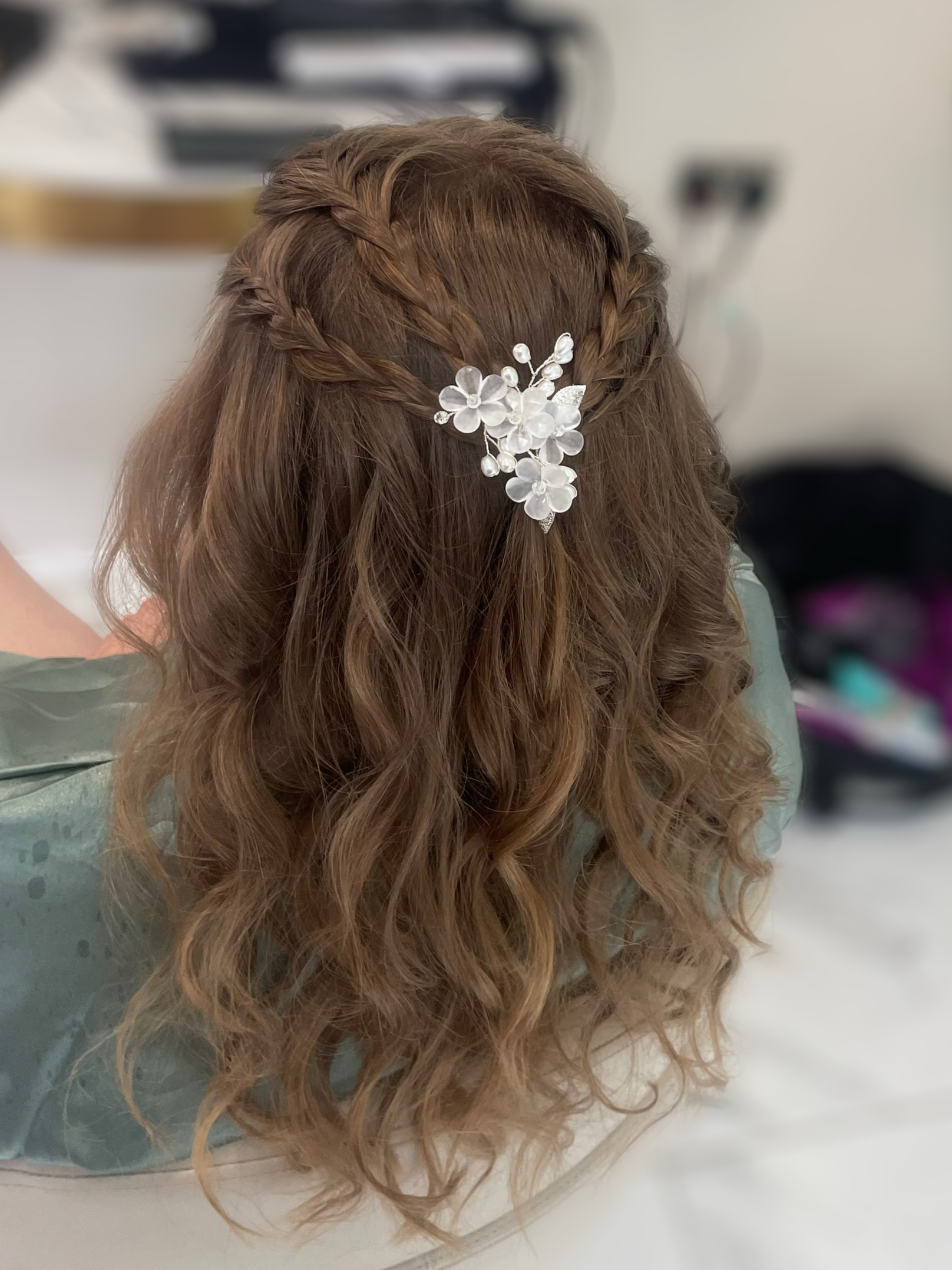 Back of a woman with wavy, light brown hair styled with two braids and a floral hair clip on the side.