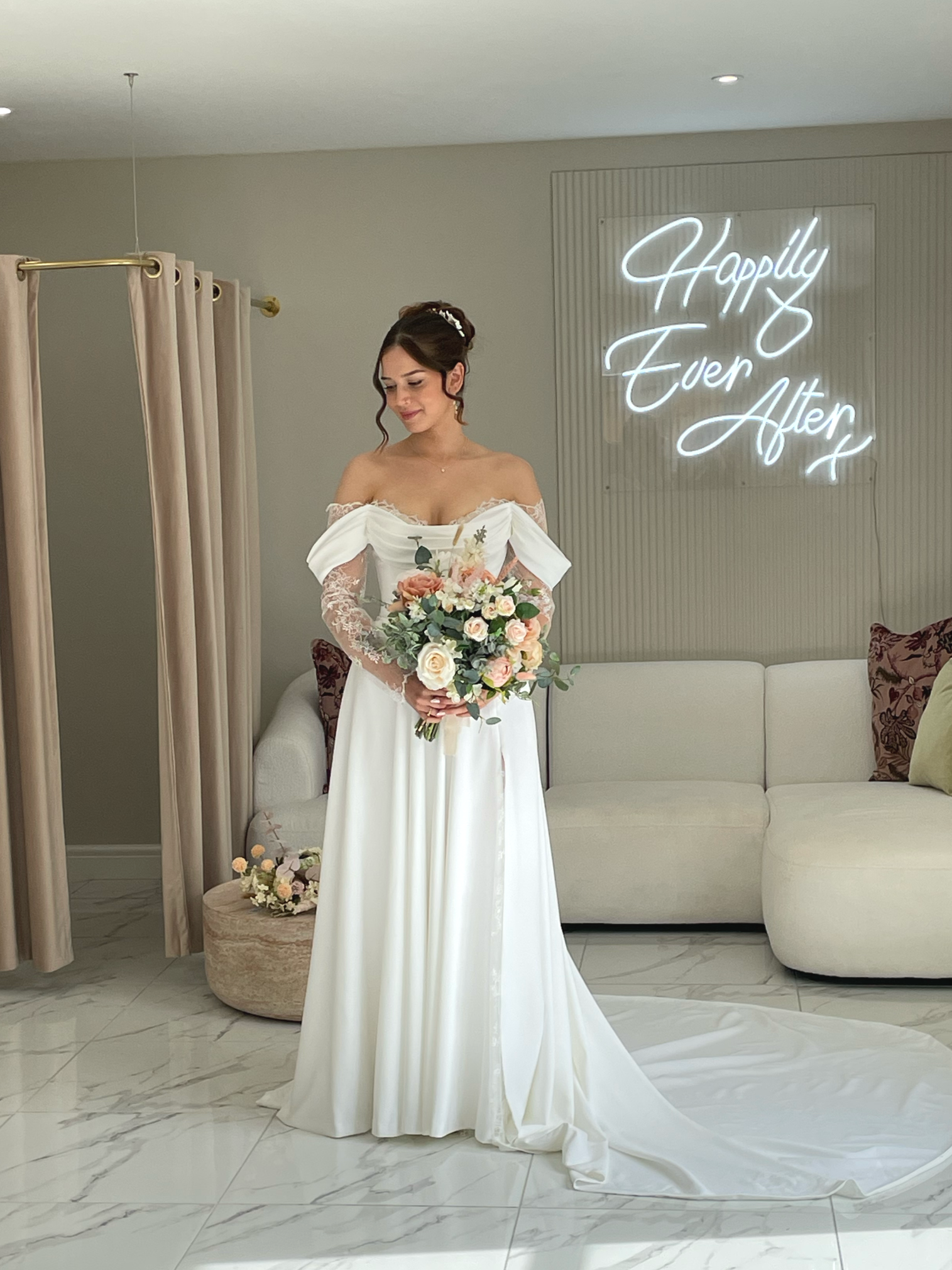 Bride in a white wedding dress holding a bouquet of flowers in a room with a neon sign that says 'Happily Ever After' in the background.