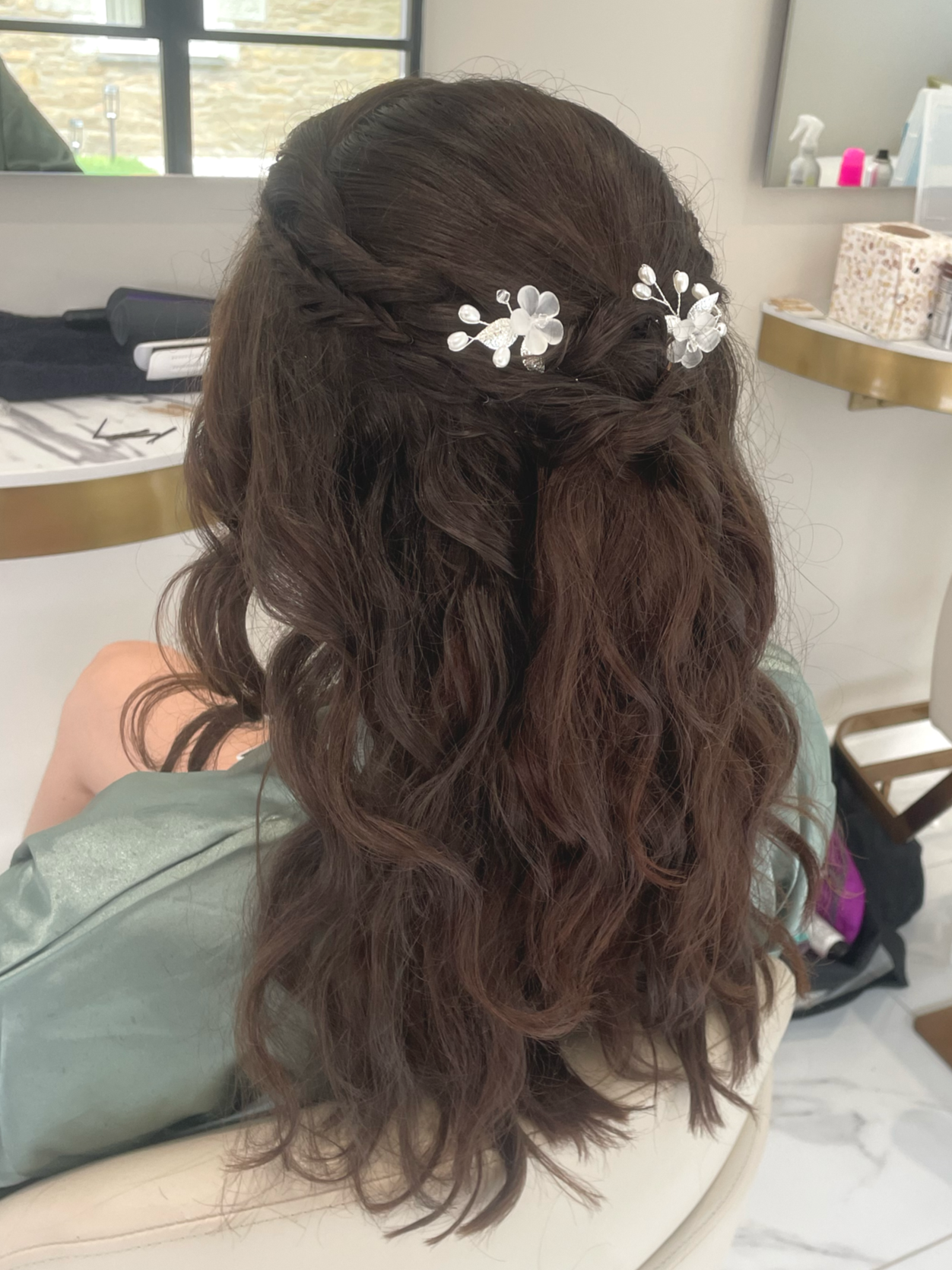 Back view of a woman with long, curly brown hair wearing floral hair accessories.