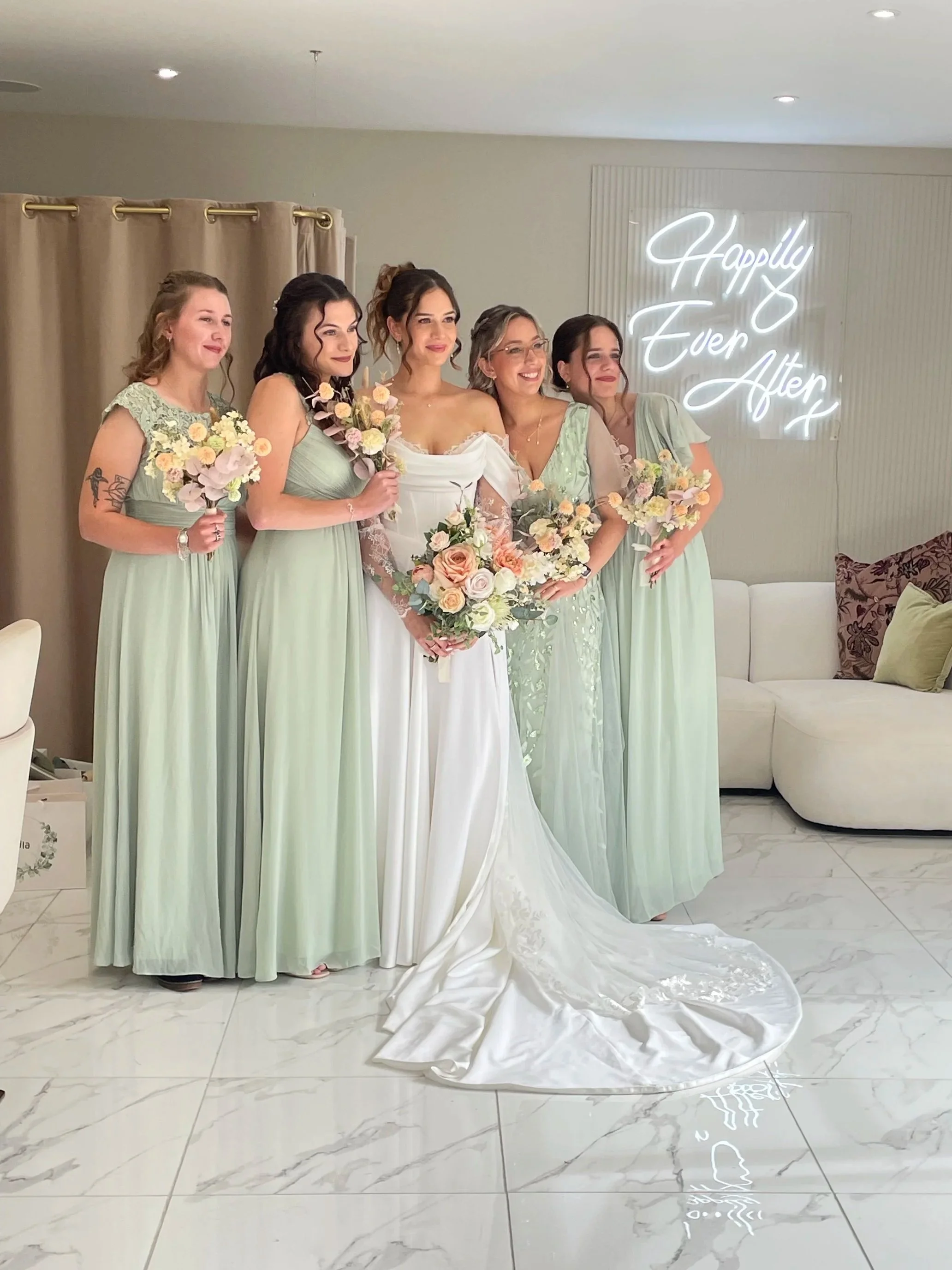 Bride with five bridesmaids in pastel green dresses holding bouquets in a wedding setting with a neon sign that reads "Happily Ever After."