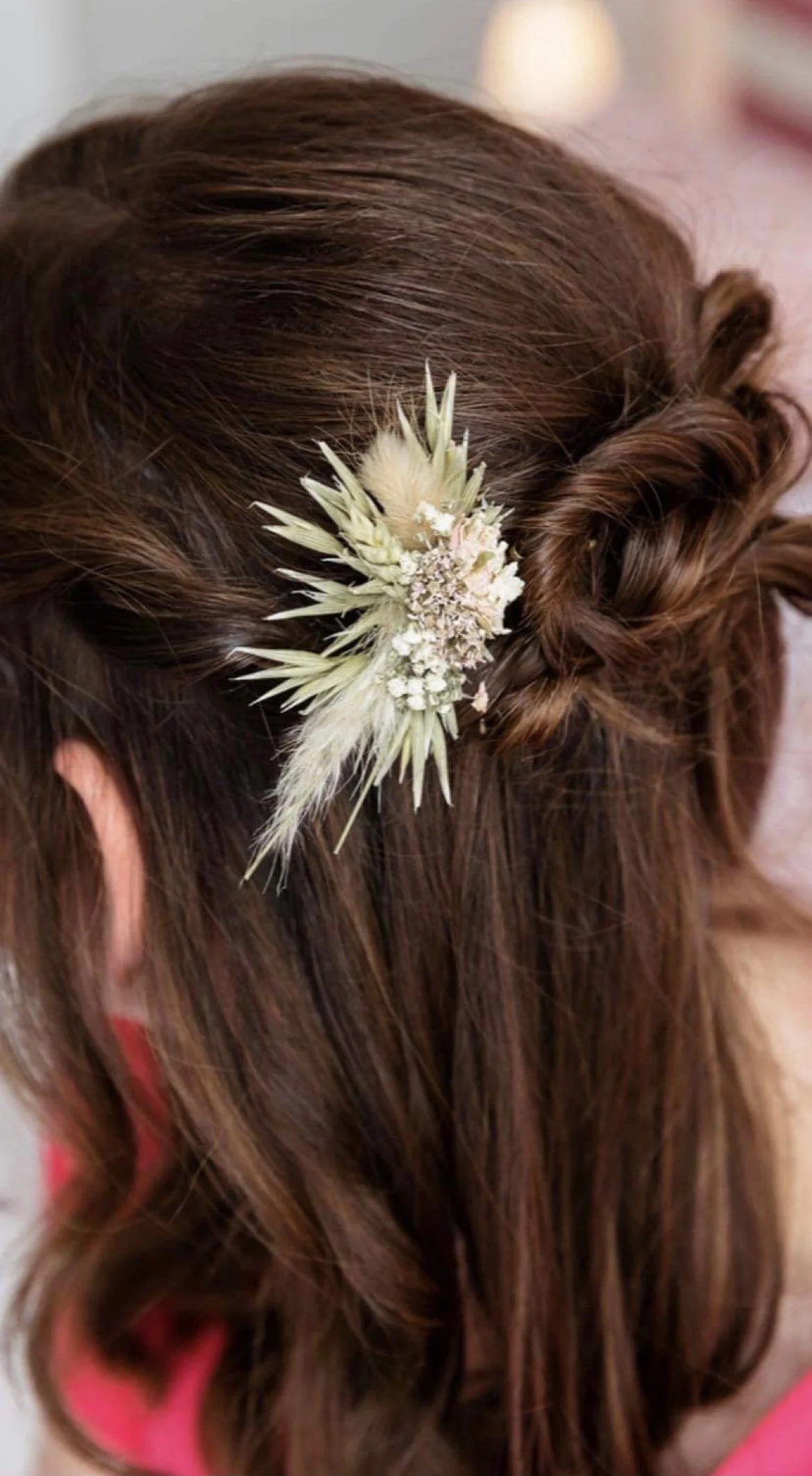 A woman's hairstyle with a floral hair accessory, featuring a braid and loose curls.