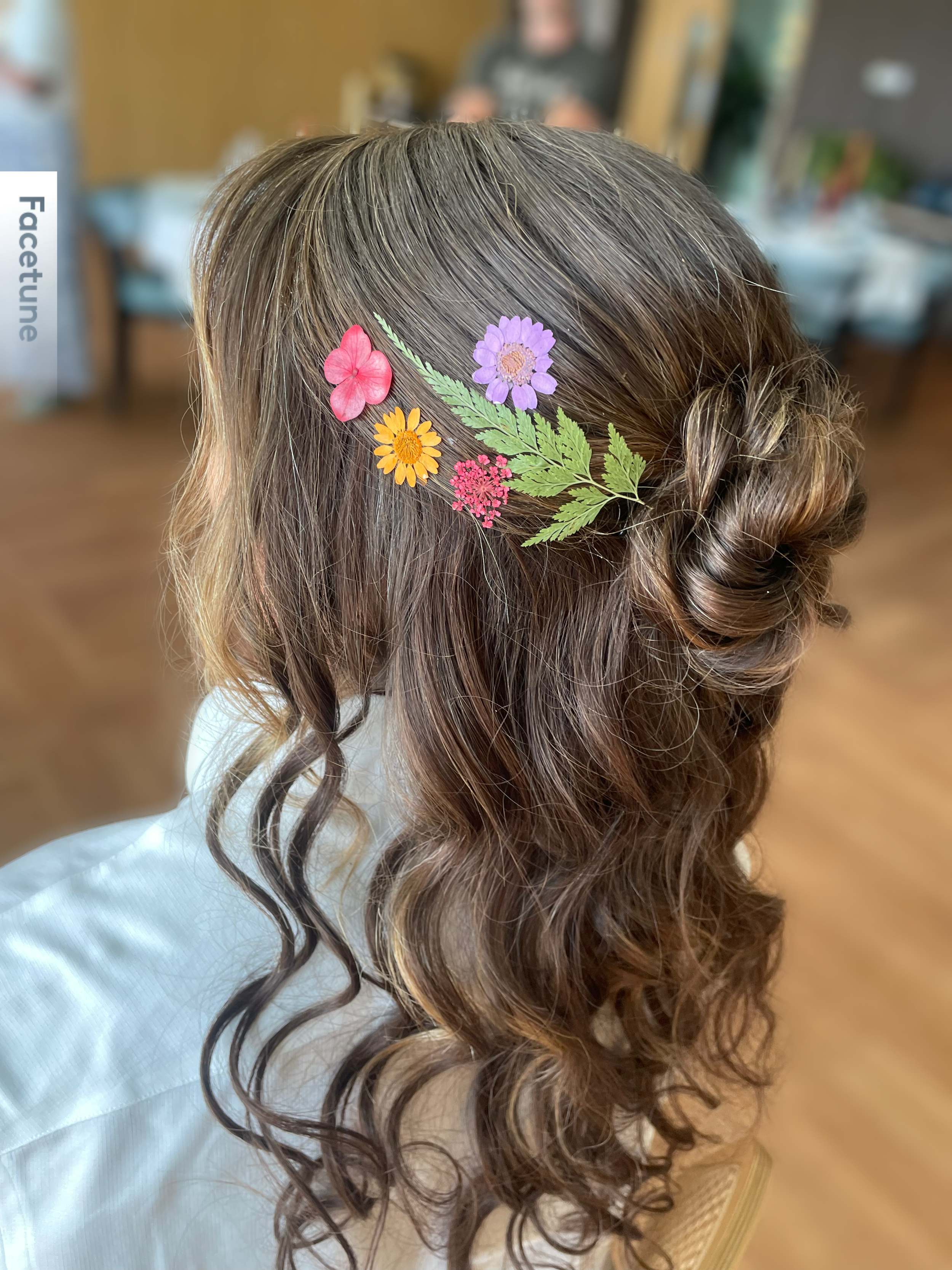 Hair tied in loose curls with a decorative floral hair clip featuring pink, purple, yellow, and red flowers and green leaves.