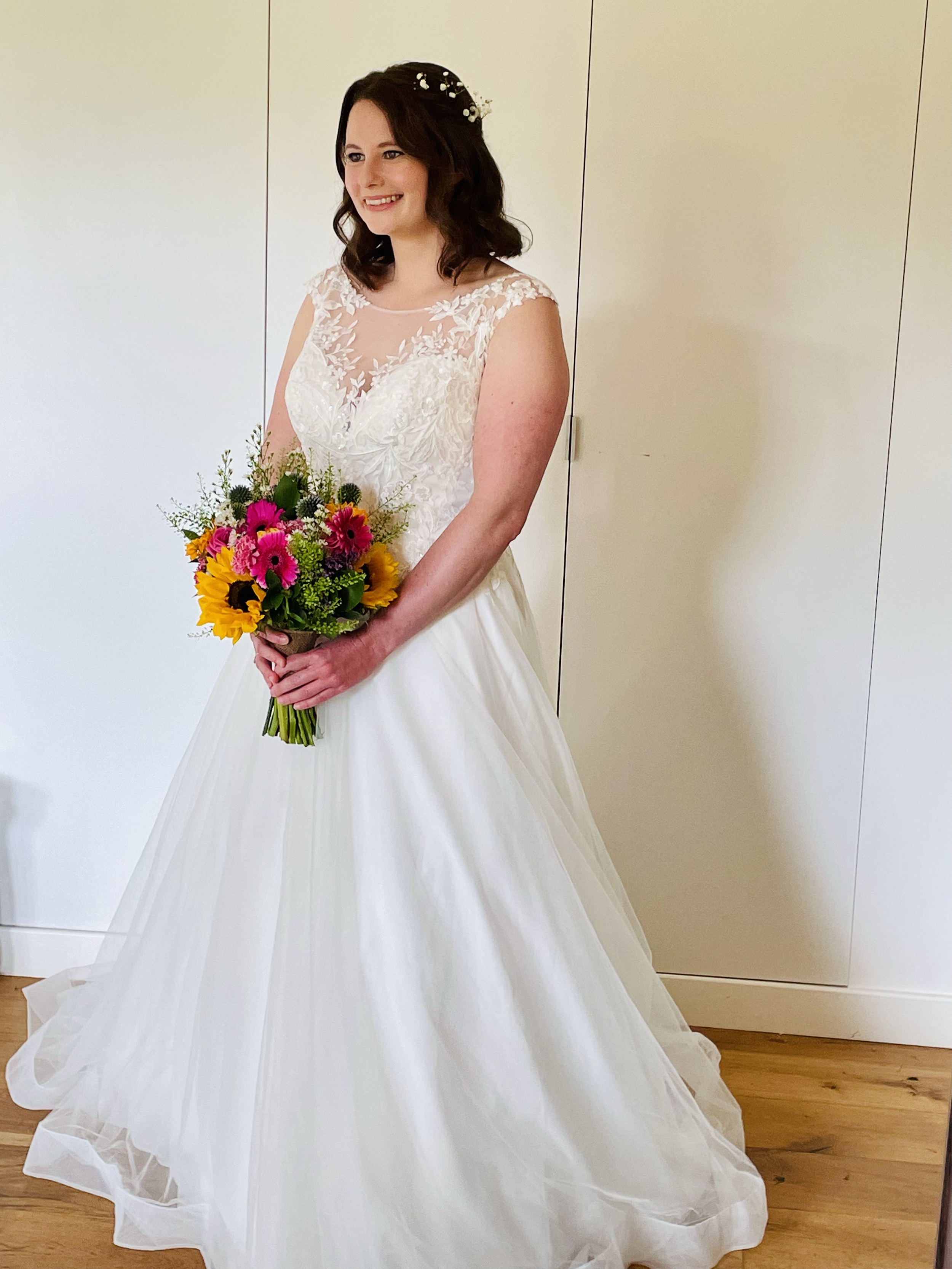 A woman in a wedding dress holding a colorful bouquet of flowers, standing indoors.