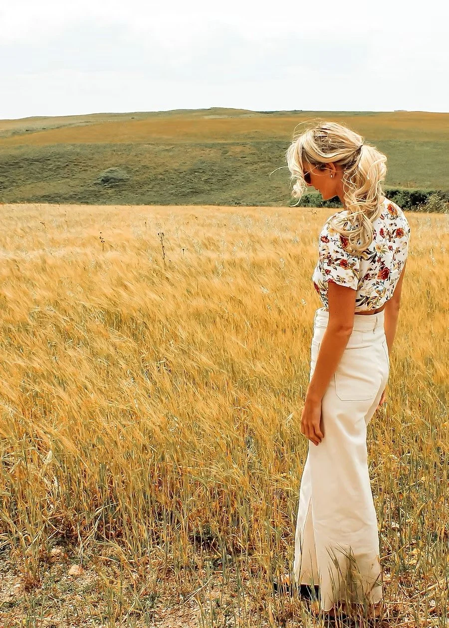 Woman sitting on a bench, writing in a notebook, with abstract artwork leaning against a wall beside her.