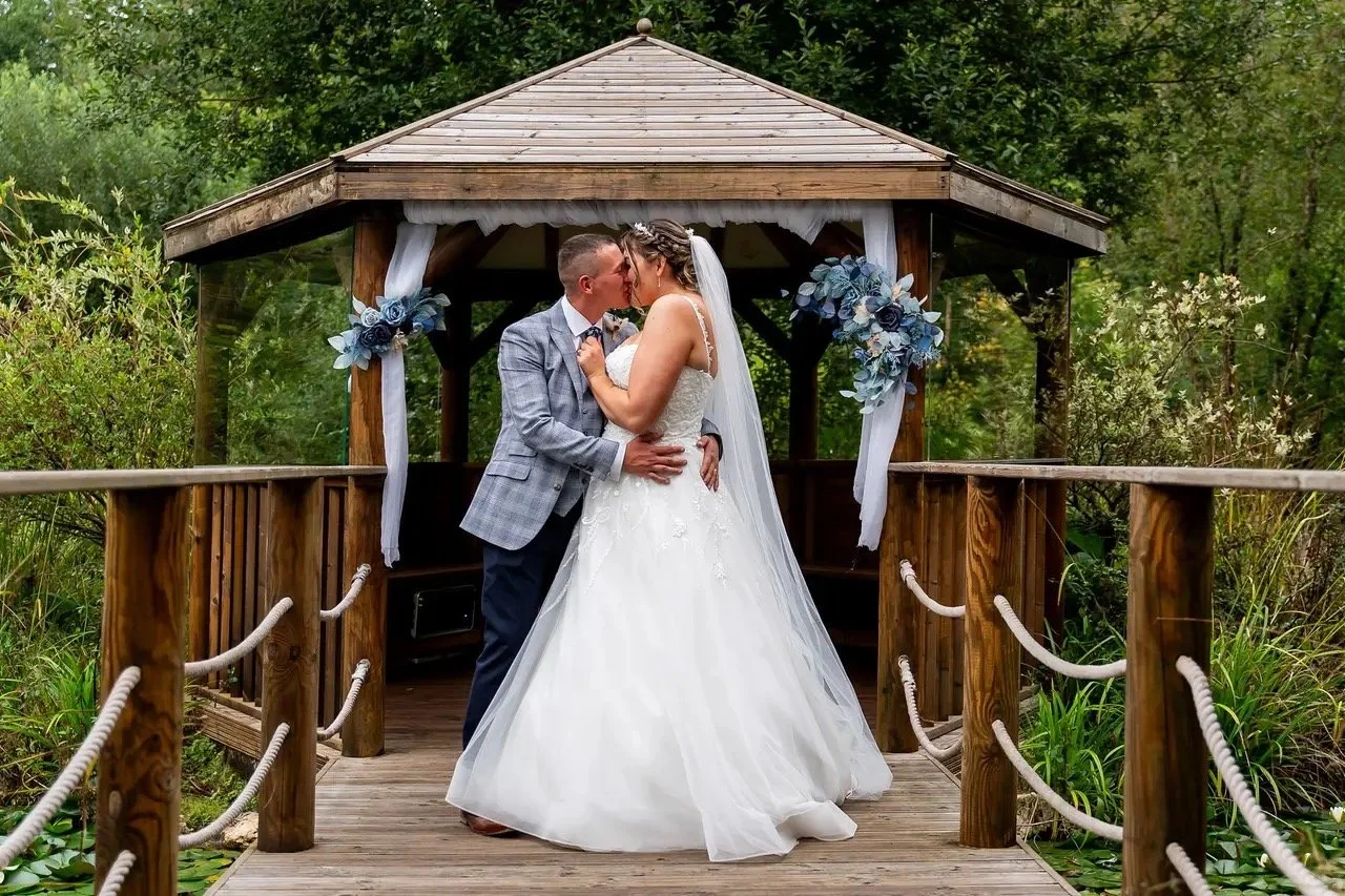 A bride and groom sharing a kiss in a gazebo surrounded by greenery during their wedding.