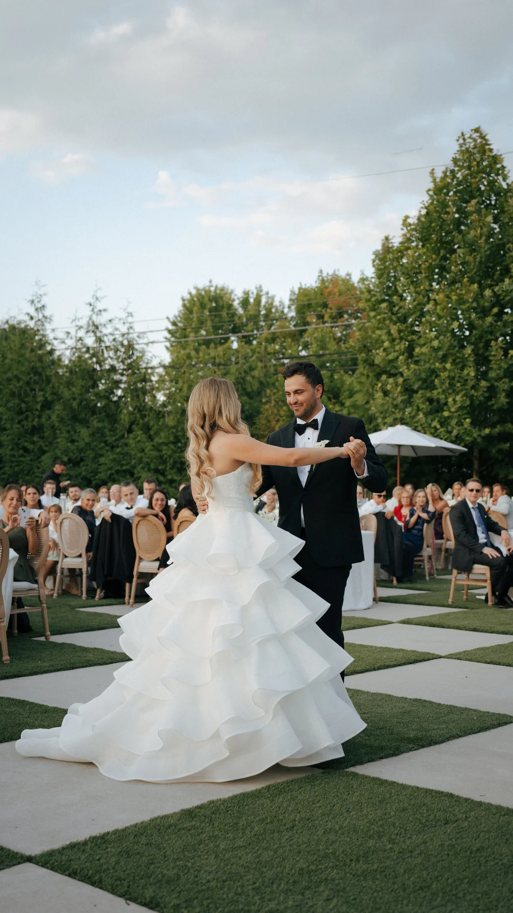 A couple together on an outdoor ceremony aisle, surrounded by seated guests.