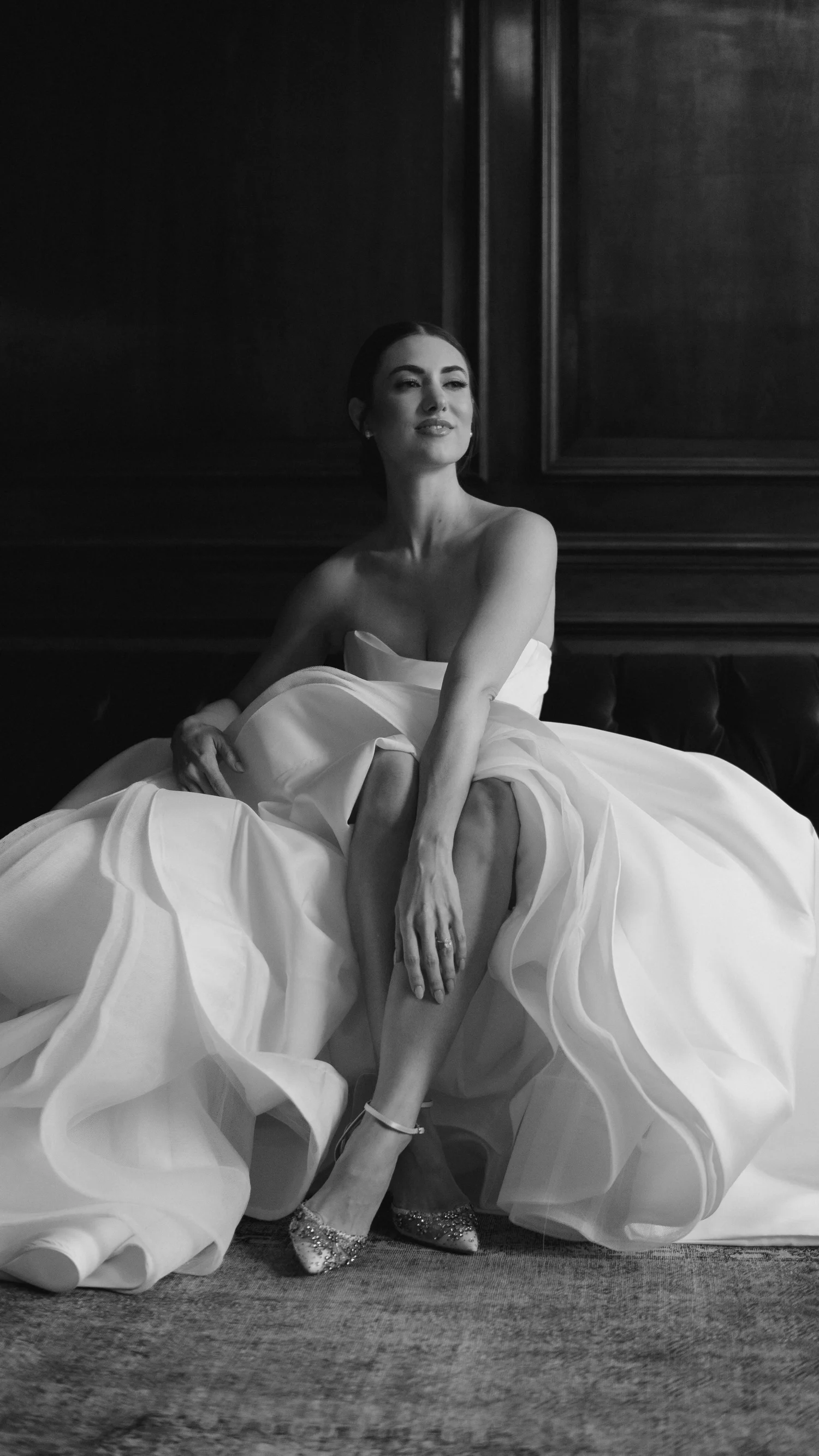 Black-and-white portrait of a bride seated in a sweeping wedding dress.