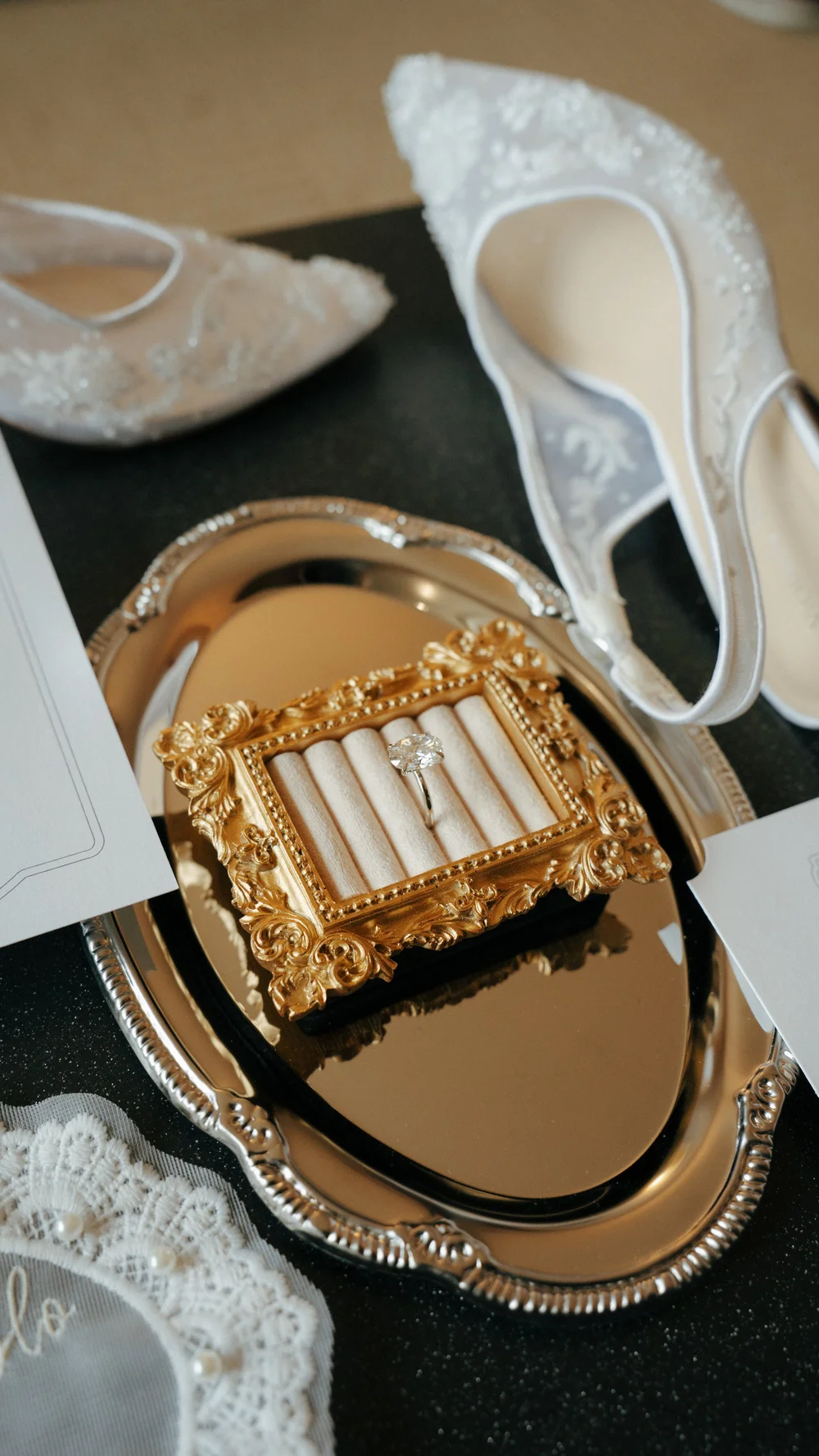 White shoes and gold bridal accessories arranged on a textured surface.