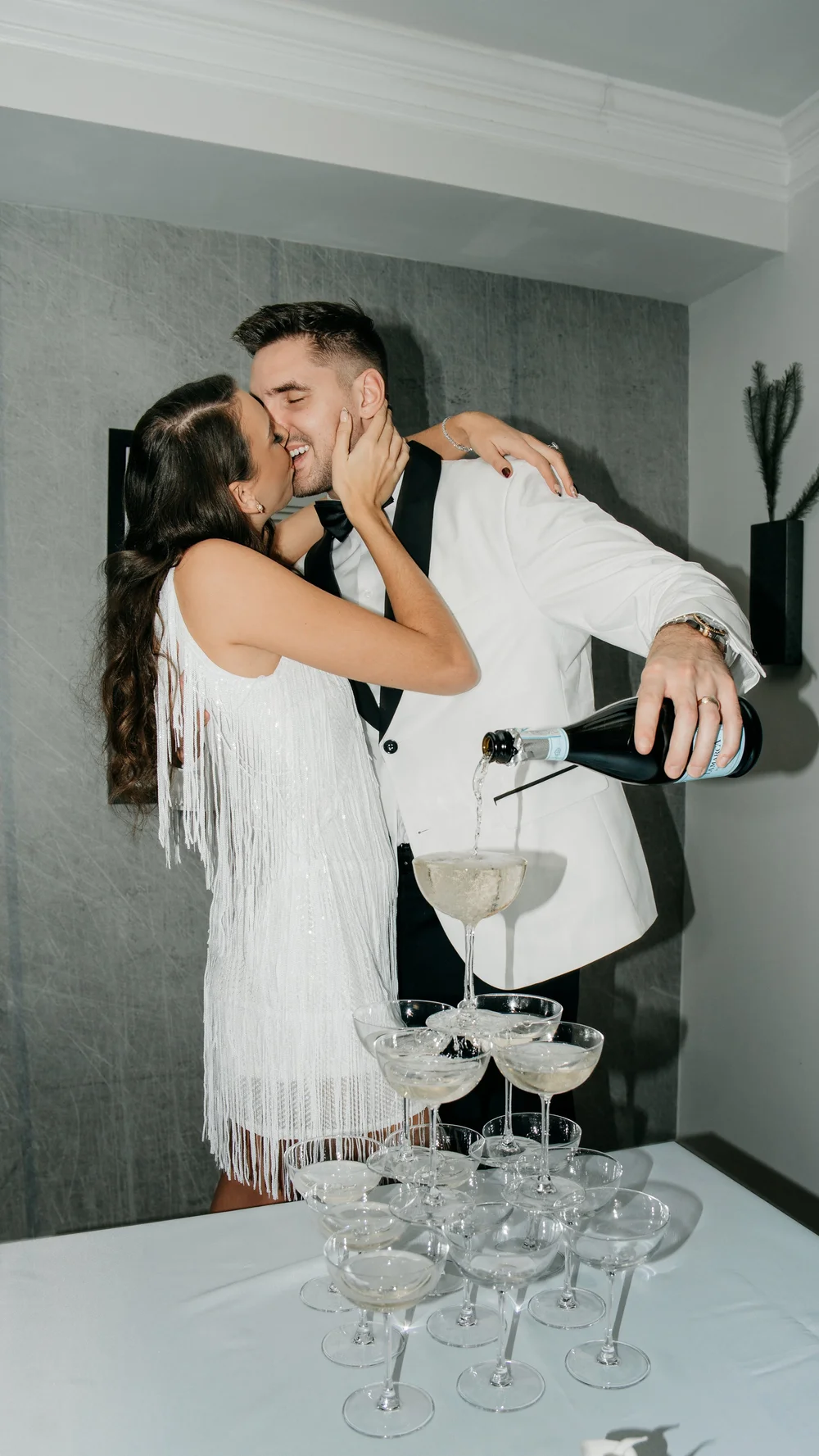 A couple embracing beside a tower of champagne glasses.