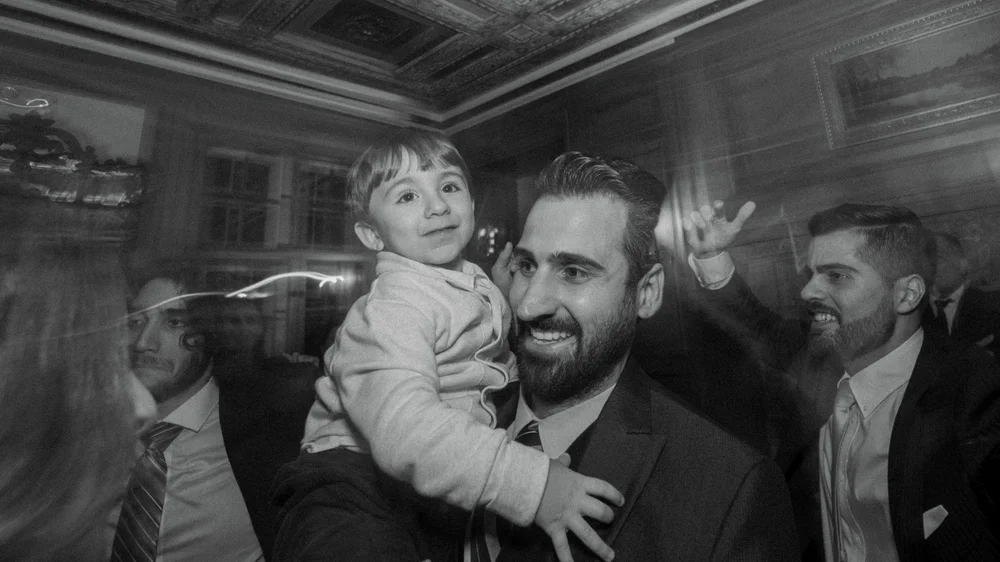 Black-and-white moment of a man holding a young child among wedding guests.