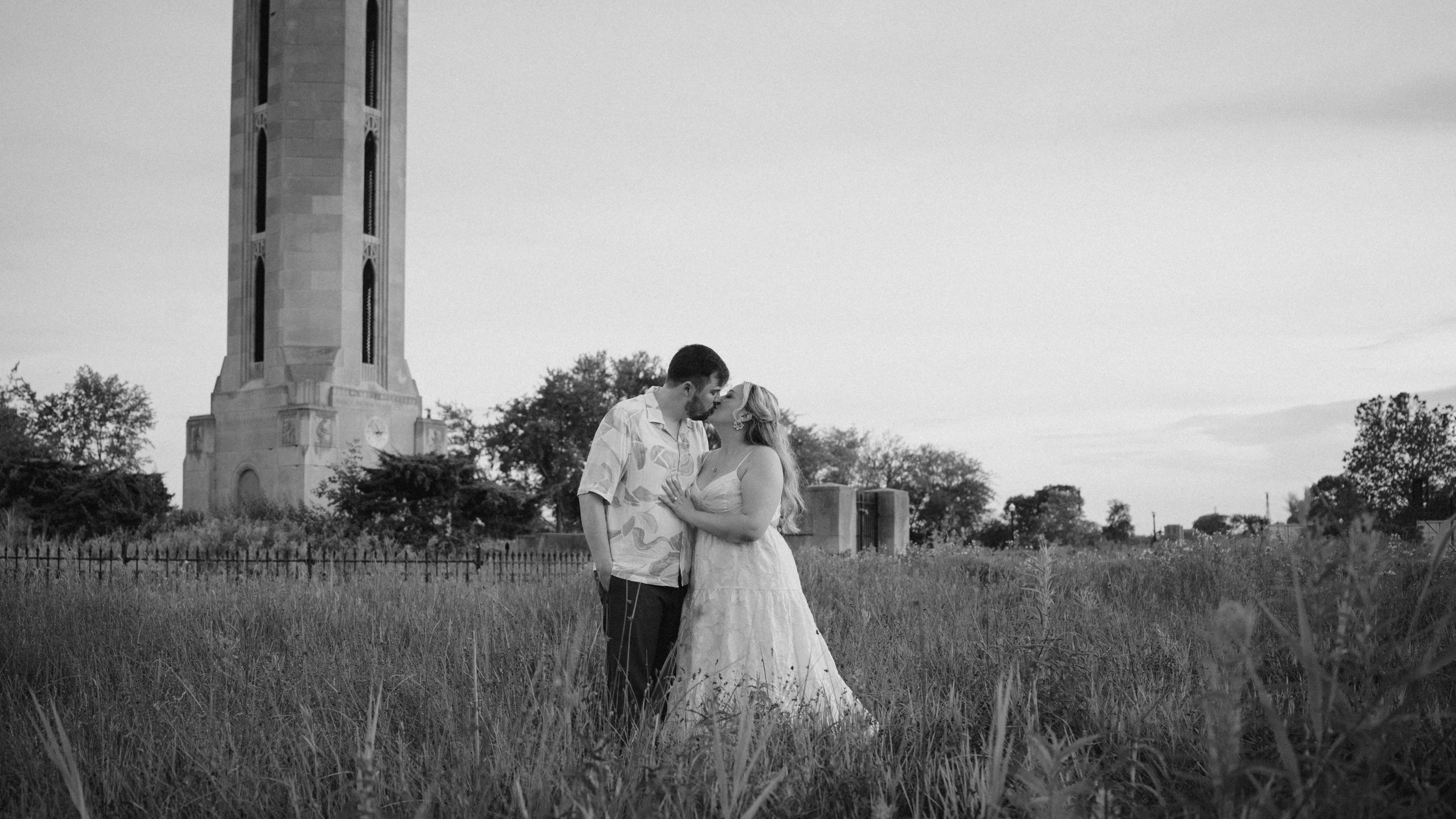 Maggie and Johnathan kissing among tall grasses on Belle Isle, with the tower behind them, photographed in black and white.