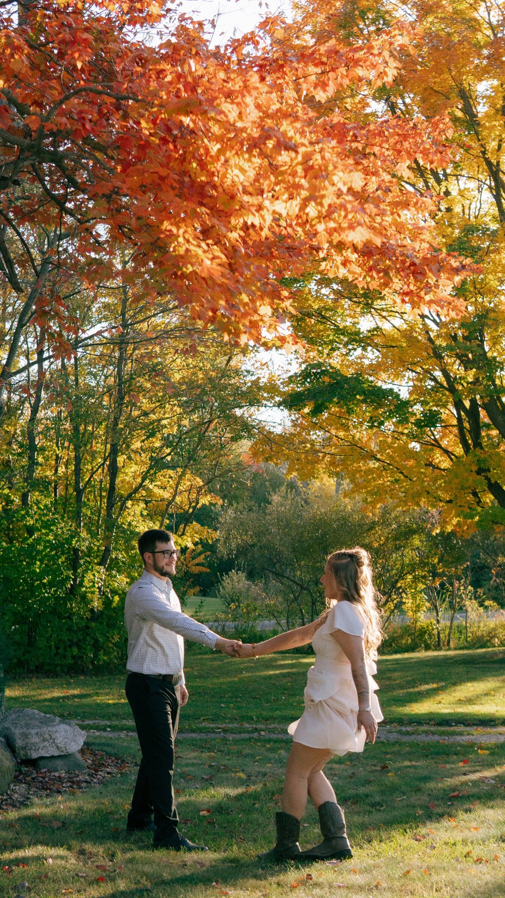 A couple holding hands beneath orange autumn leaves.