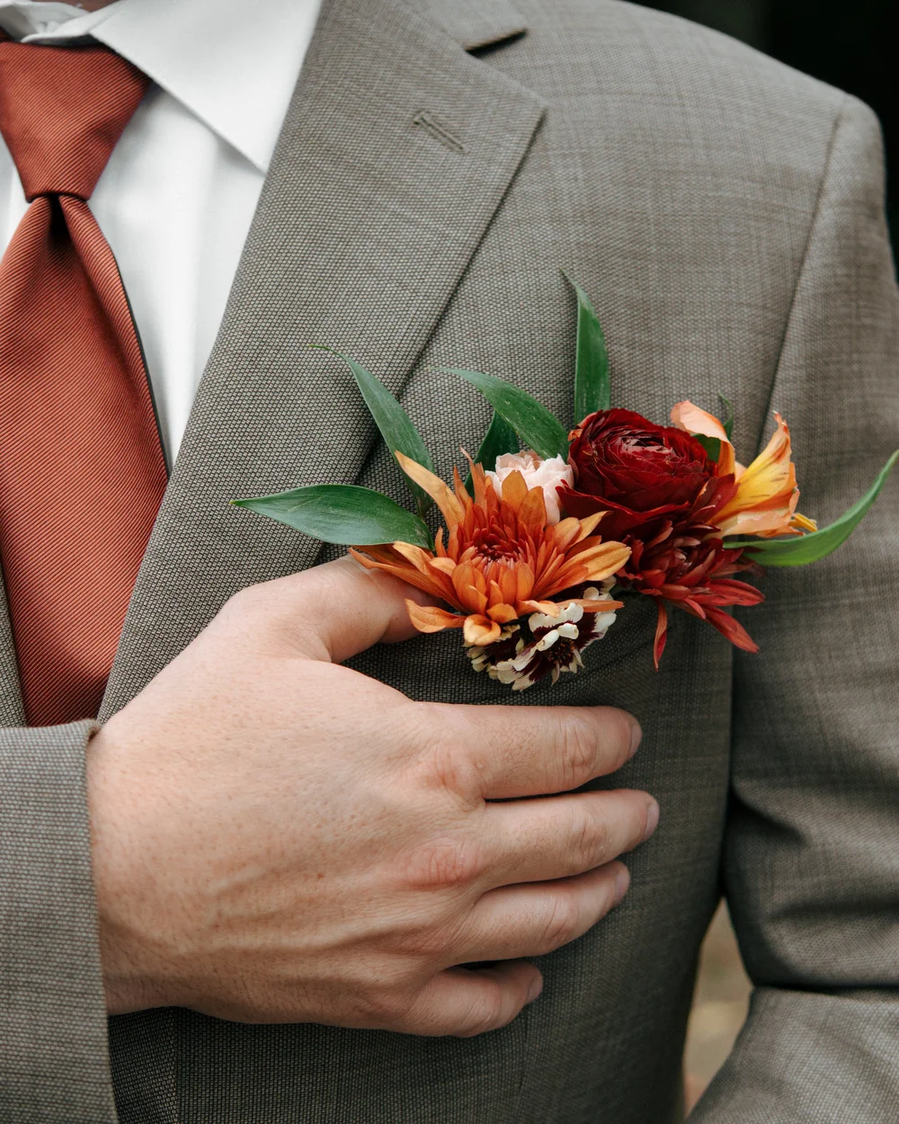 Orange flowers pinned to a gray suit with a rust-colored tie.