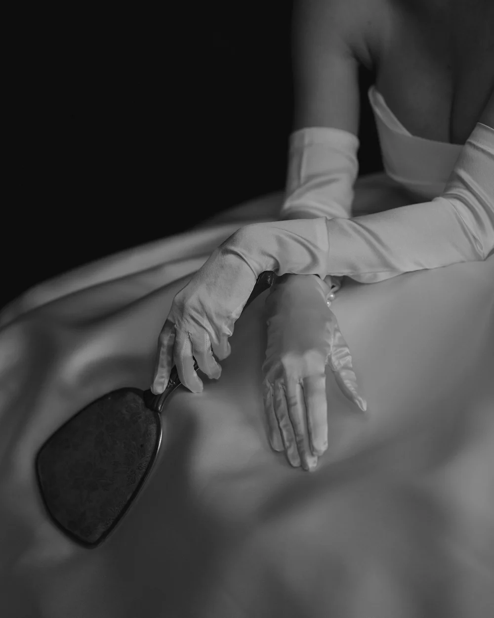Black-and-white detail of a bride’s hands resting on satin fabric.