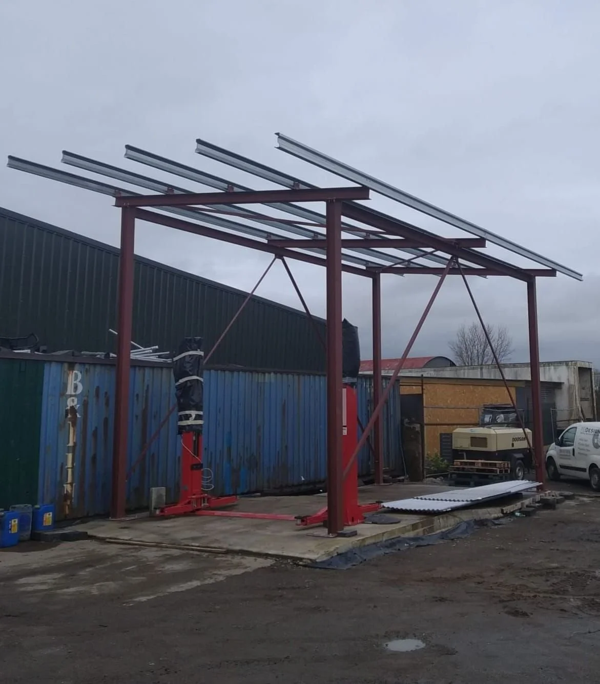 Steel frame structure under construction on a concrete platform with underground cables and construction equipment nearby.