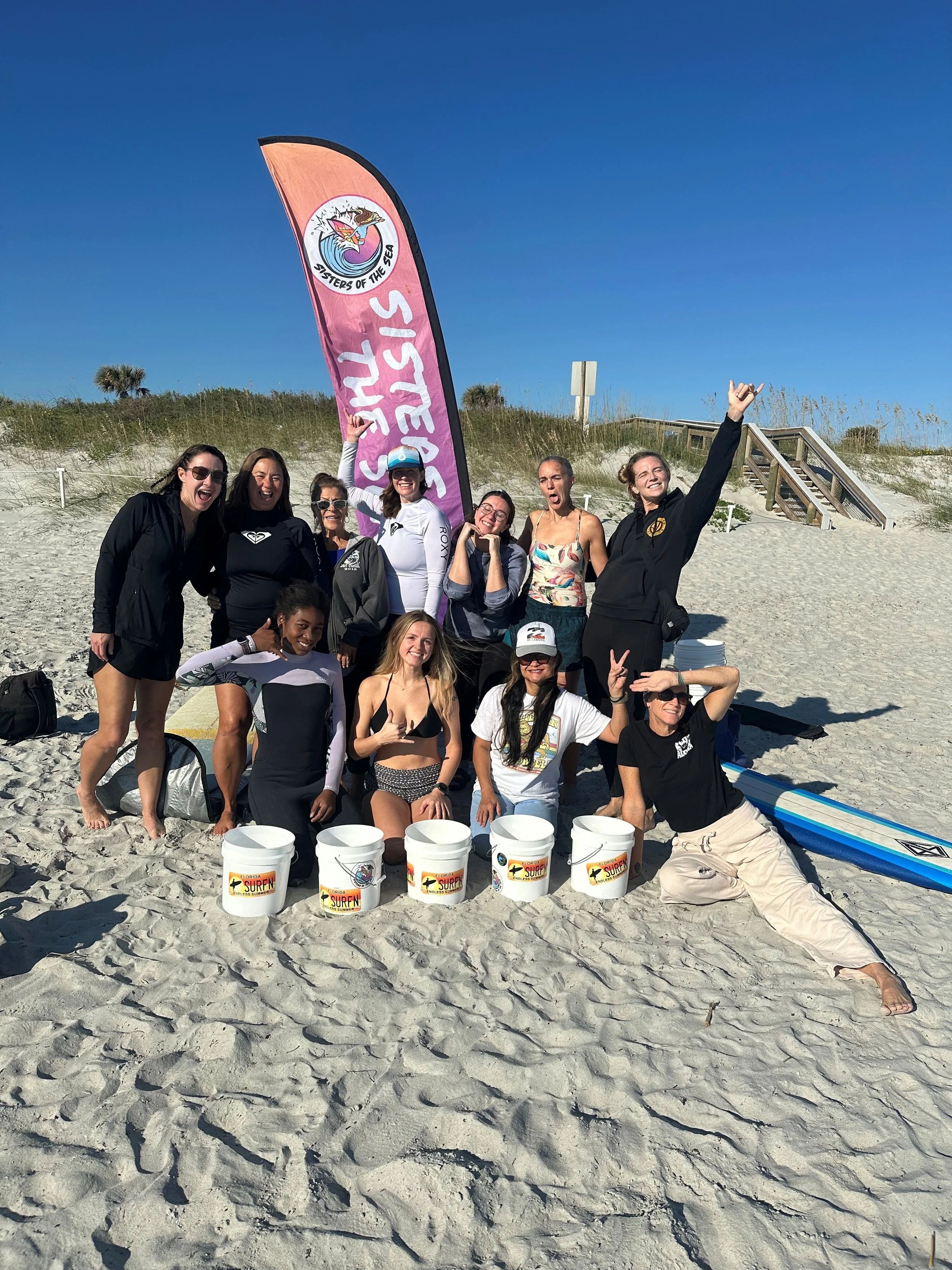 Group of women on the beach smiling for a photo and about to surf