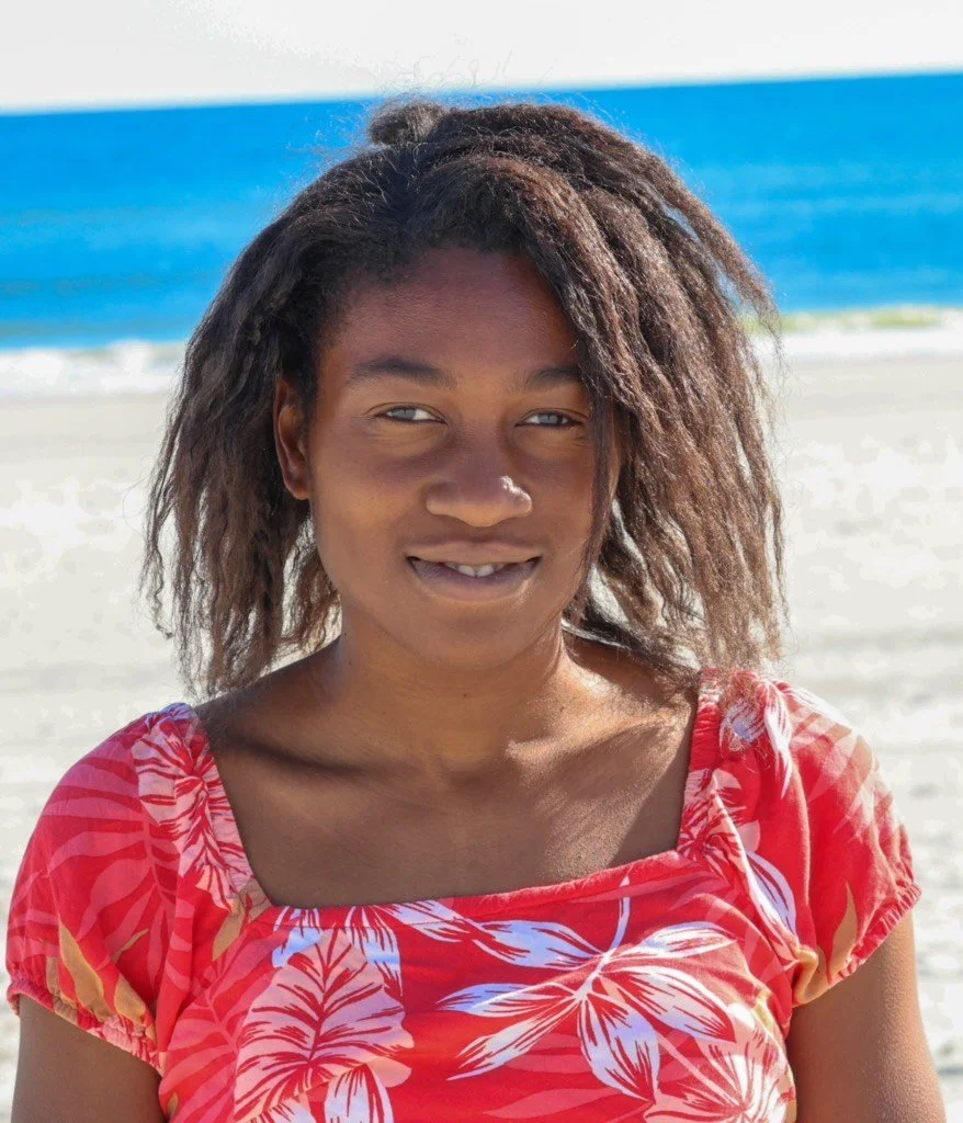 Young woman with curly hair smiling on the beach.