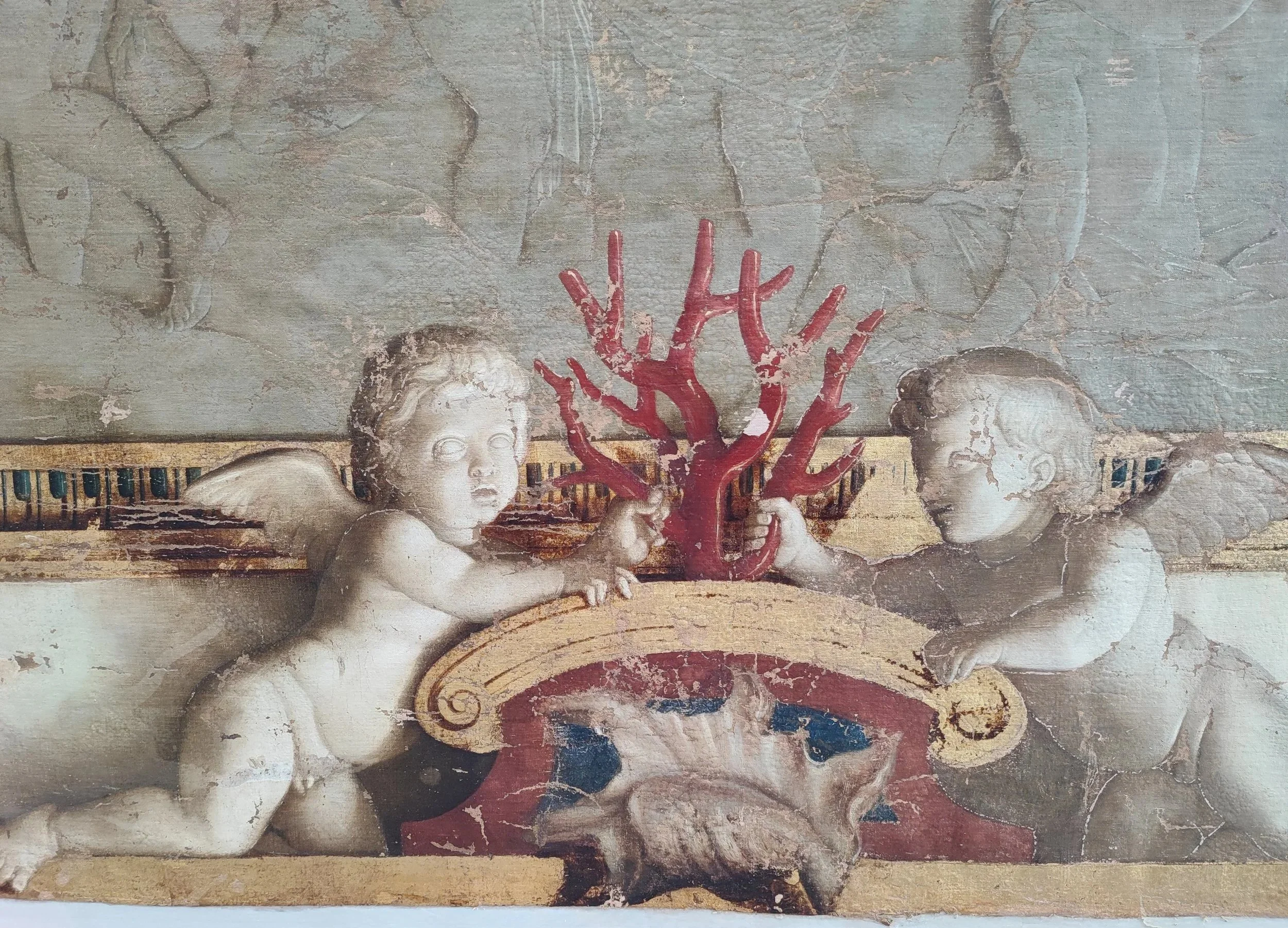 Deux anges en relief, un rouge et un blanc, tenant une branche rouge, dans un décor classique avec une toile de fond endommagée.
