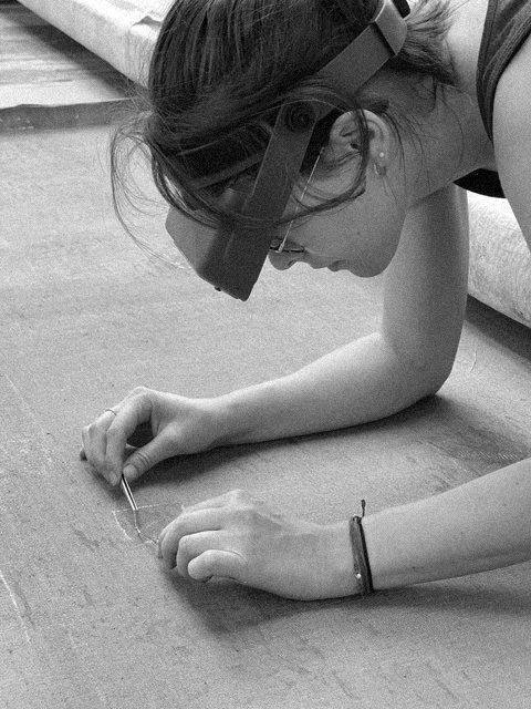 Une personne portant des lunettes de protection examine une pièce ou un échantillon sur un tapis ou un plan de travail.