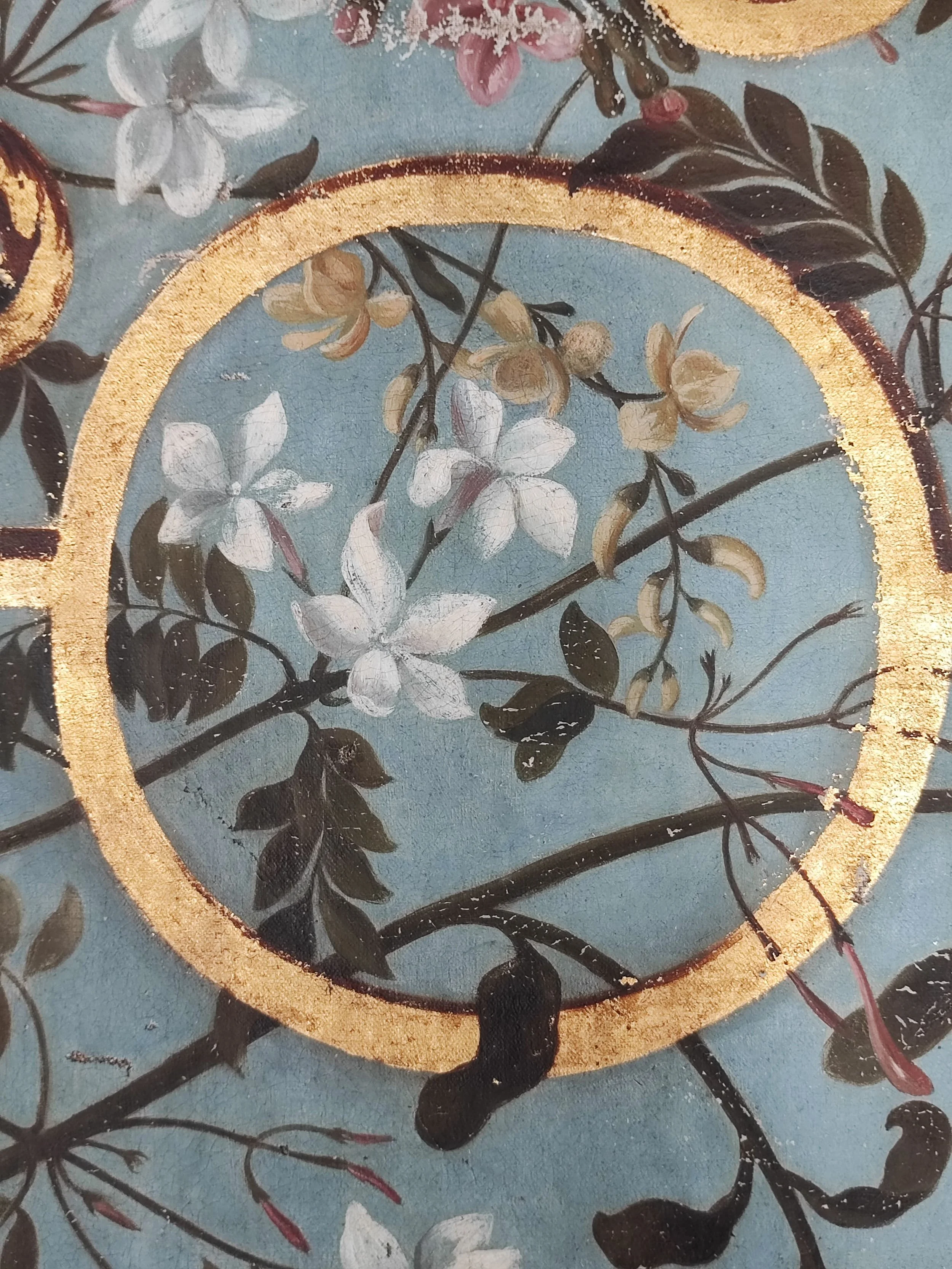 Détail d'une peinture ou fresque représentant des branches avec des fleurs blanches et jaunes, entourées d'un cercle doré.