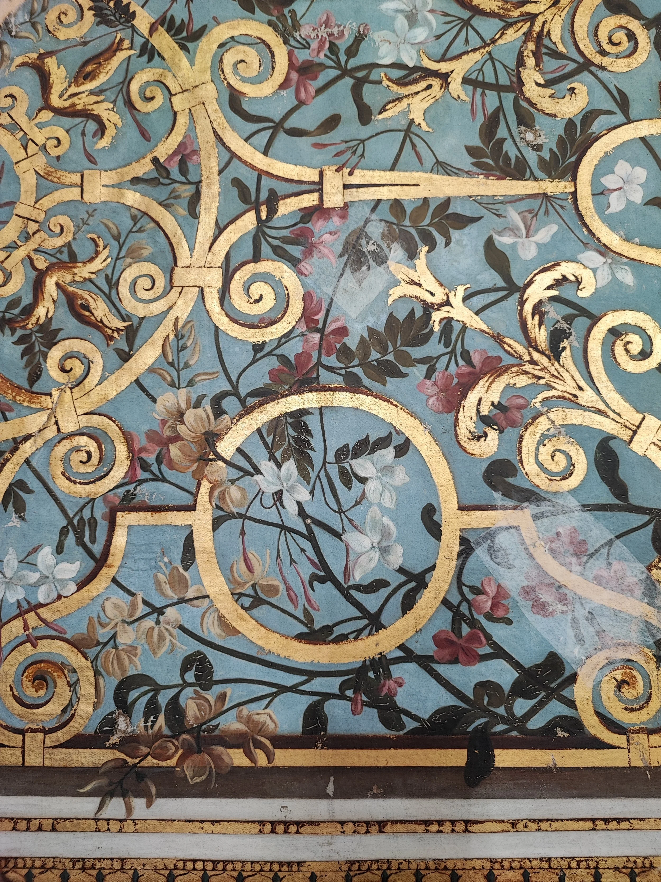 Détail d'une décoration en or avec des motifs floraux et des branches contre un fond turquoise.