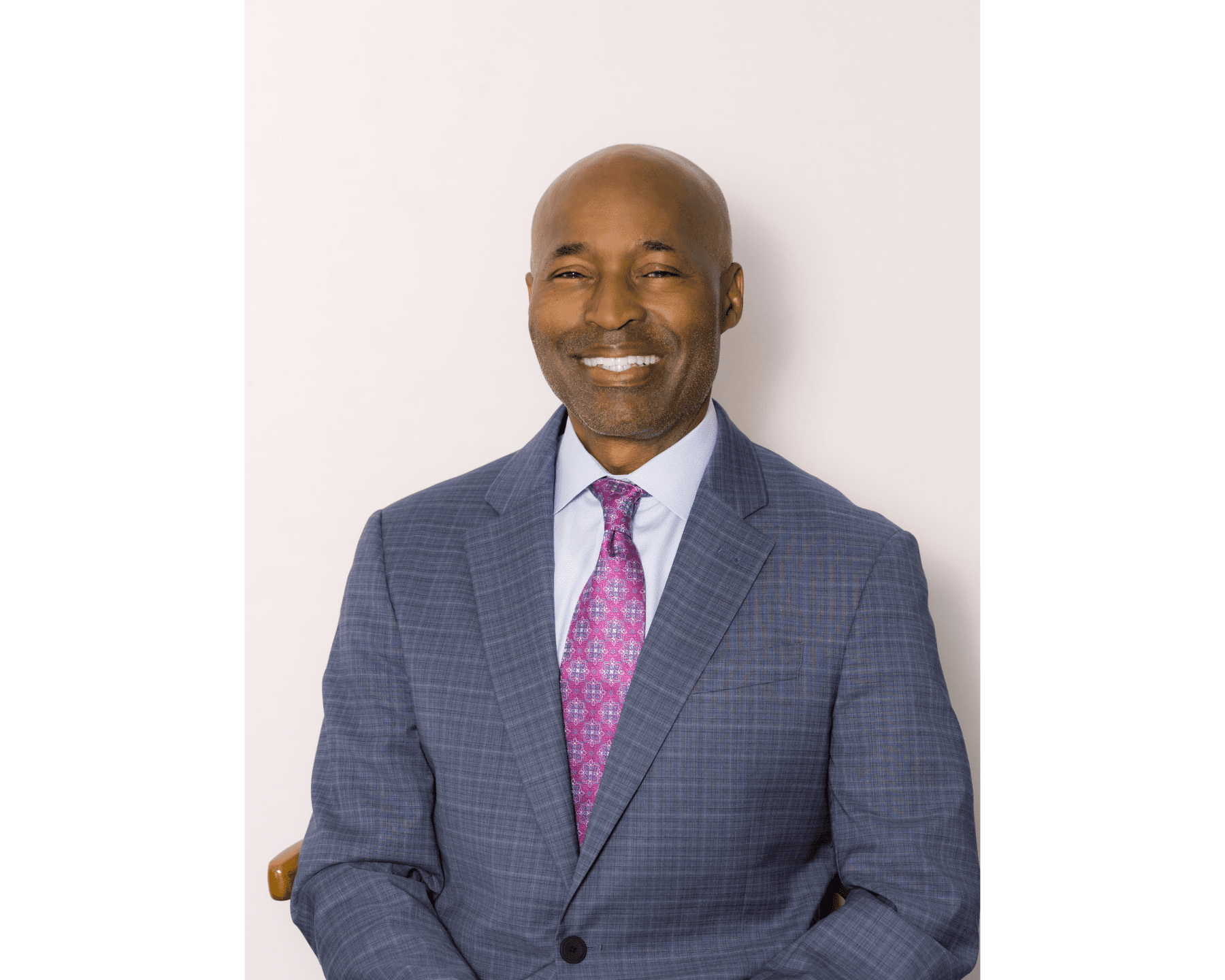 A smiling African American man in a suit and tie, sitting against a plain white background.