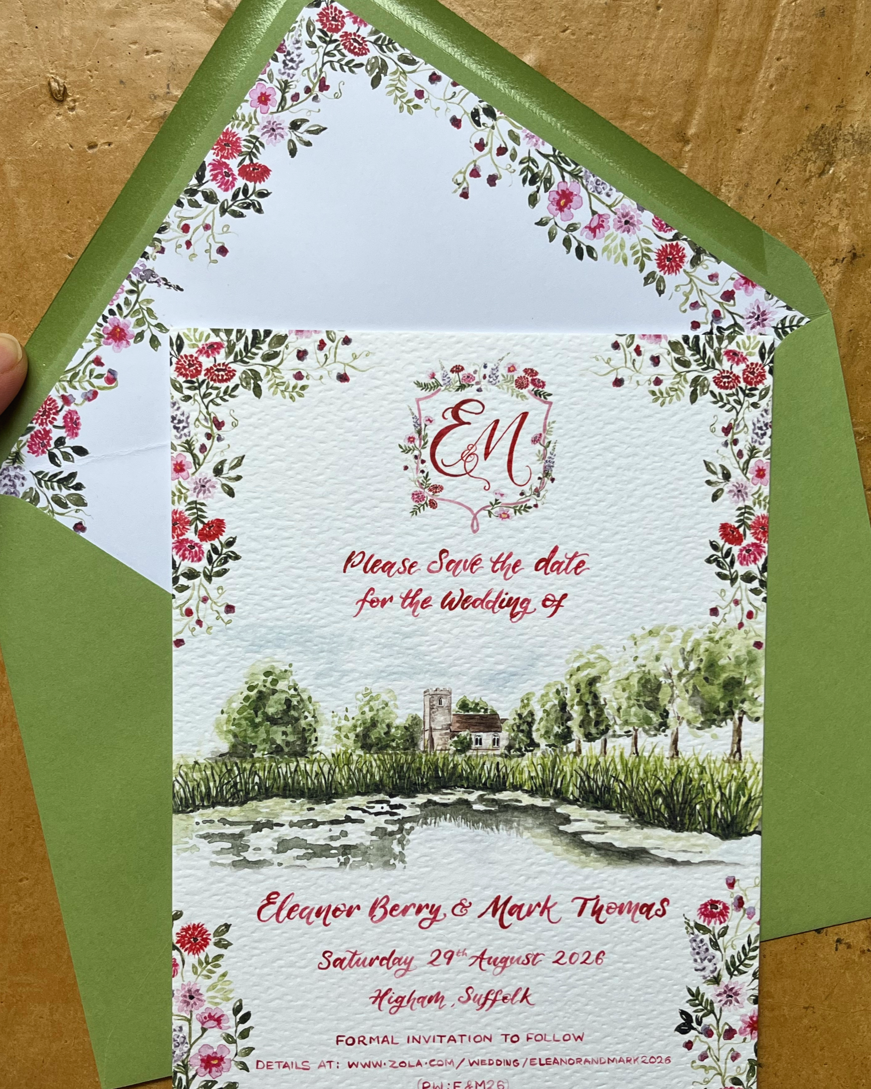 A wedding invitation with floral border, featuring a watercolor illustration of a church and trees near a pond. Text includes the initials 'E & M,' the names Eleanor Berry and Mark Thomas, the date August 29, 2026, and location Higham, Suffolk.
