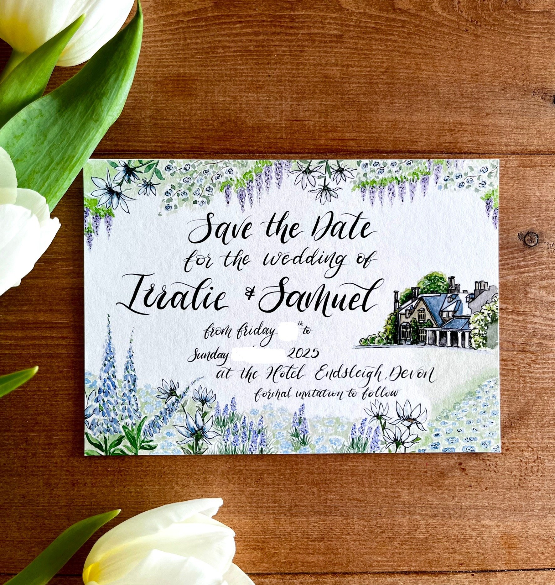 Save the date wedding invitation for Iralie and Samuel with floral illustrations and a drawing of a house, placed on a wooden surface with white tulips nearby.