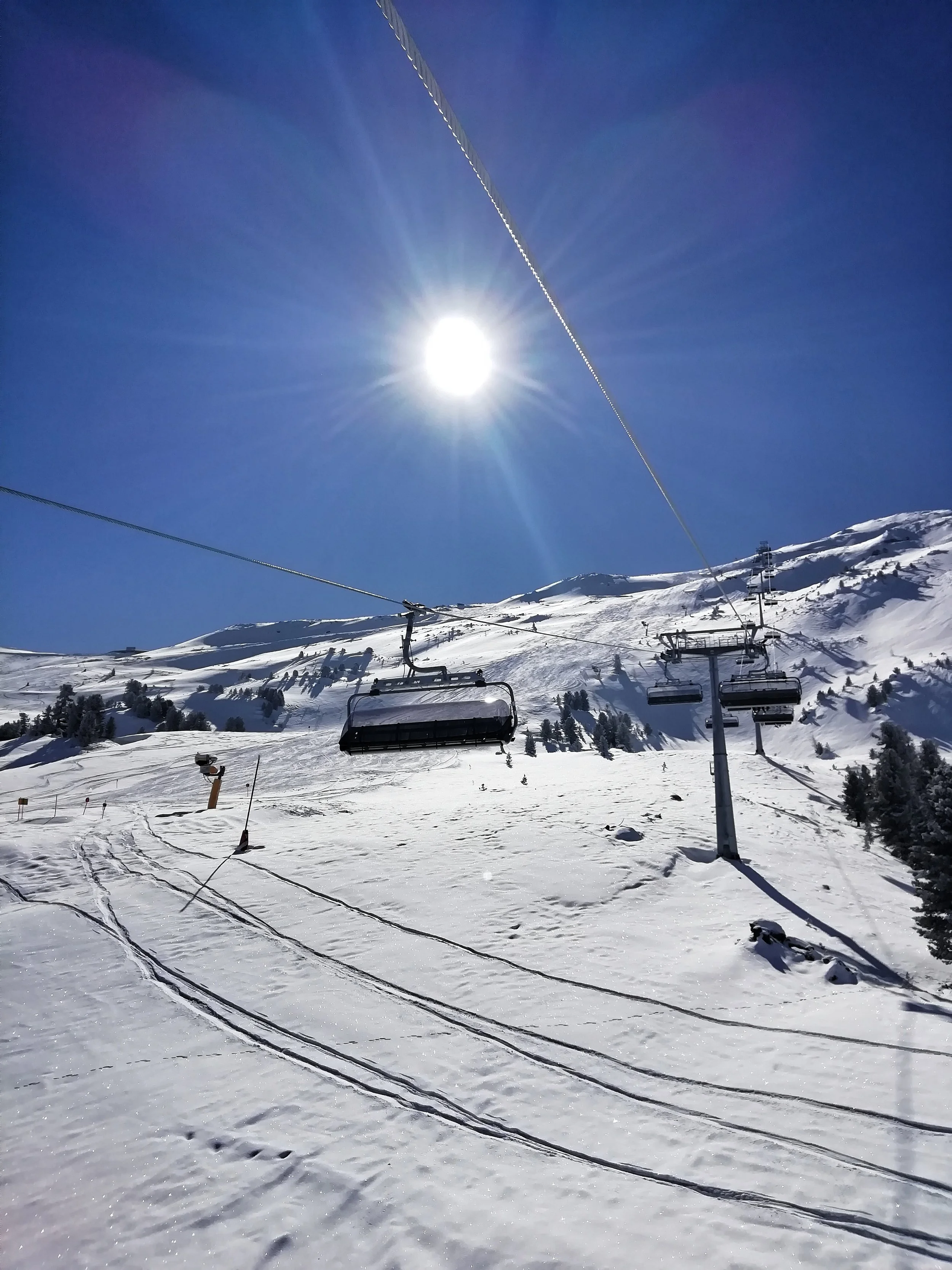 Schneebedeckte Skiliftanlagen in den Bergen bei strahlendem Sonnenschein und klar blauem Himmel.