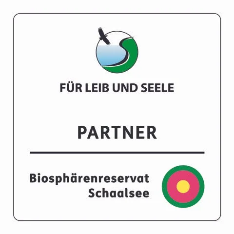 Sogenanntes "Leib und Seele" Partner-Logo, welches den Veranstaltungsort als Partner Biosphärenreservat Schaalsee kennzeichnet. Oben mit einer kleinen Weltkugel, die den See und die Umgebung andeuten soll.