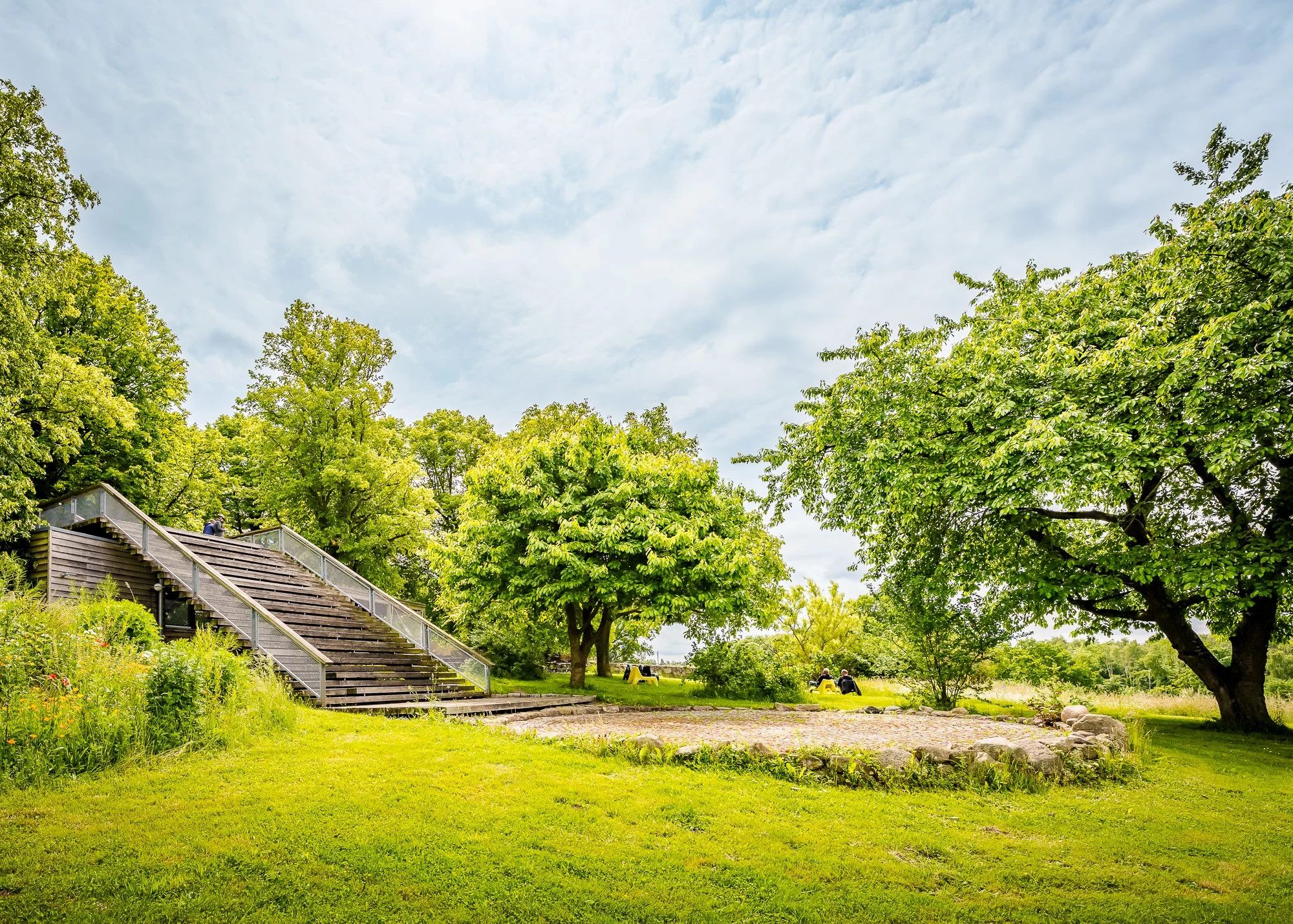 Grüner Park mit Bäumen, Stufen and Liegen, bei schönem Wetter.