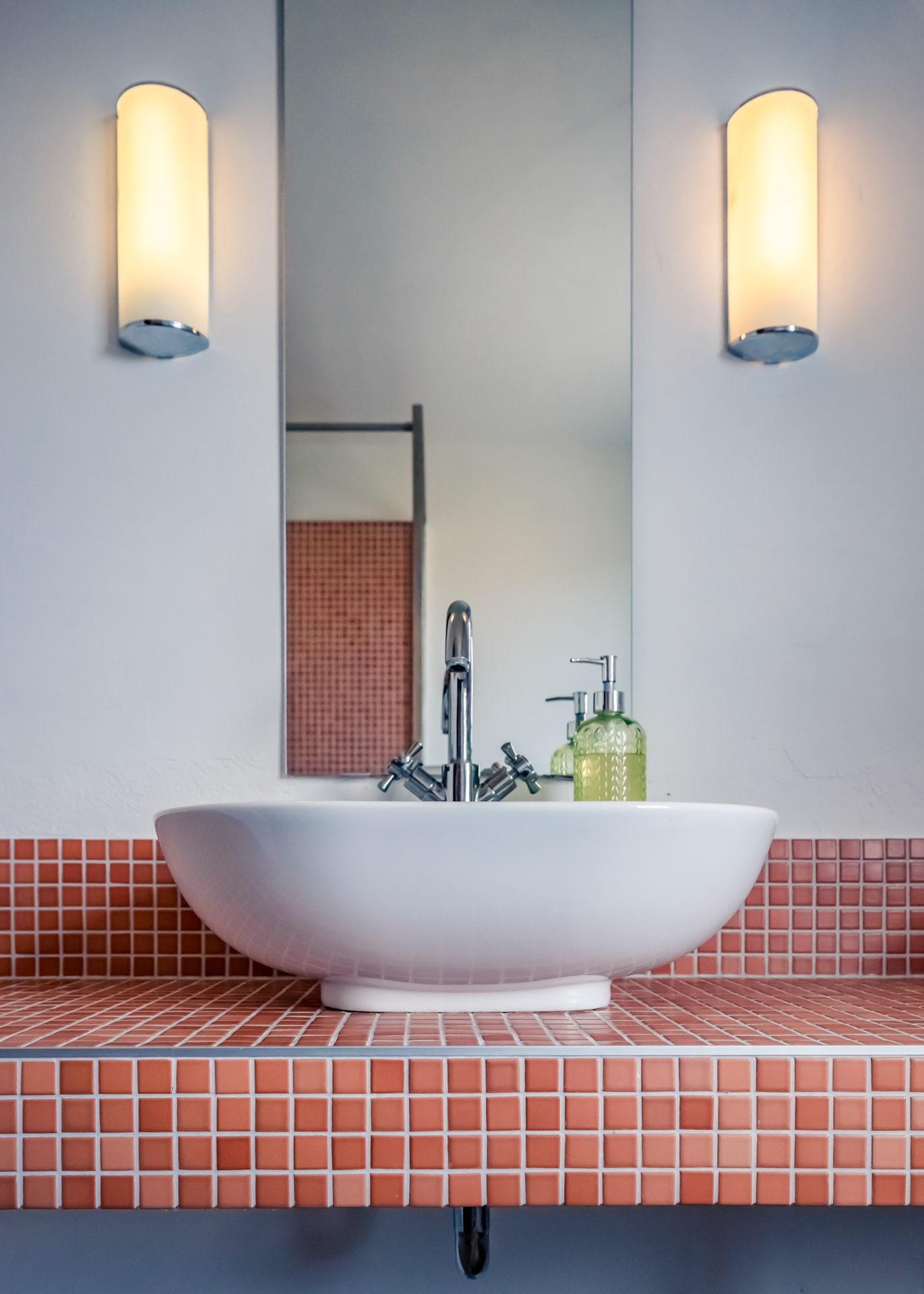 Waschbecken mit Spiegel, zwei Wandleuchten und Seifenspender.