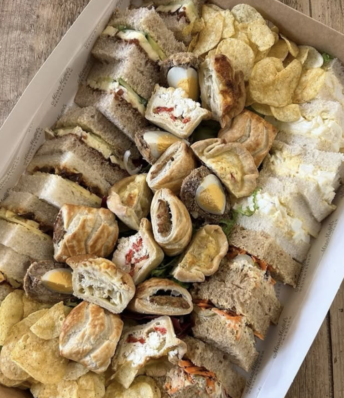 A tray of assorted finger foods including sandwiches, stuffed eggs, pinwheels, and potato chips. Tewkesbury catering and picnics.