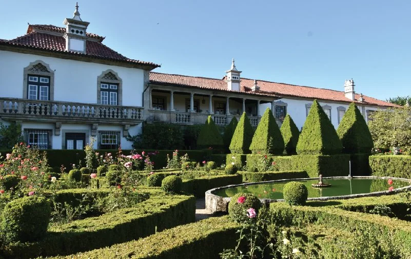 Imagem de um palácio ou mansão com jardim bem cuidado e plantas decorativas
