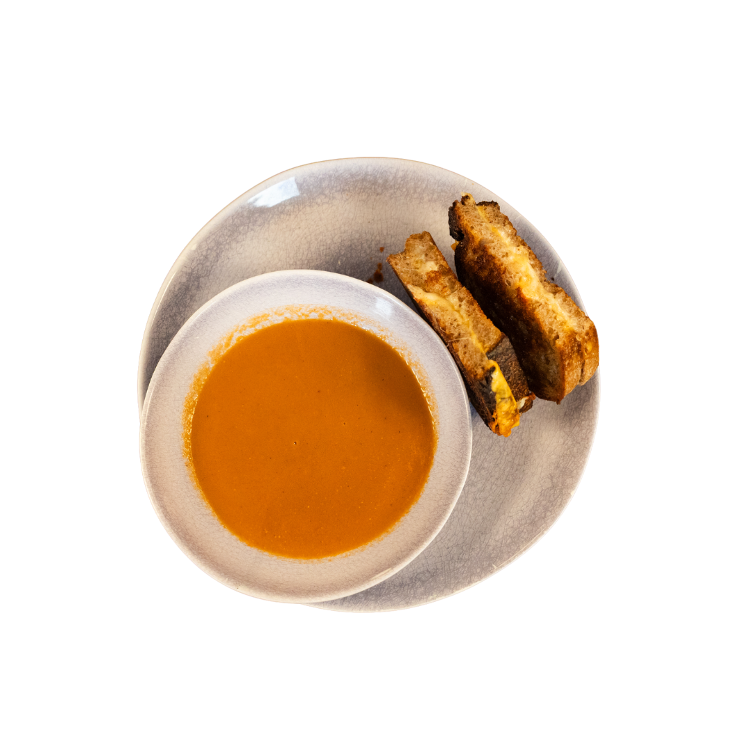 A bowl of tomato soup with grilled cheese on a plate.
