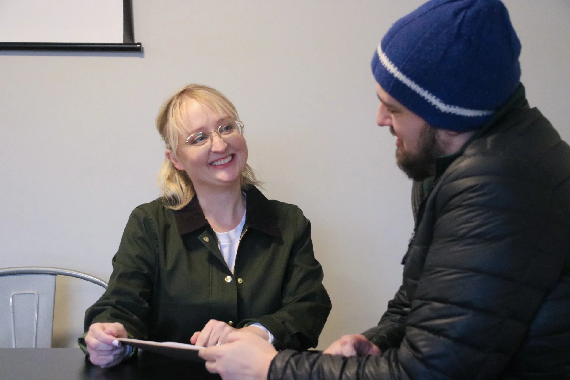 Candidate Aisha Elmquist in a green jacket talking to a young man in a hat.
