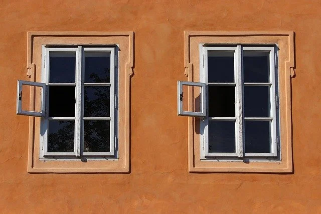 Zwei Fenster an einer orangefarbenen Wand, eines ist offen, das andere geschlossen.
