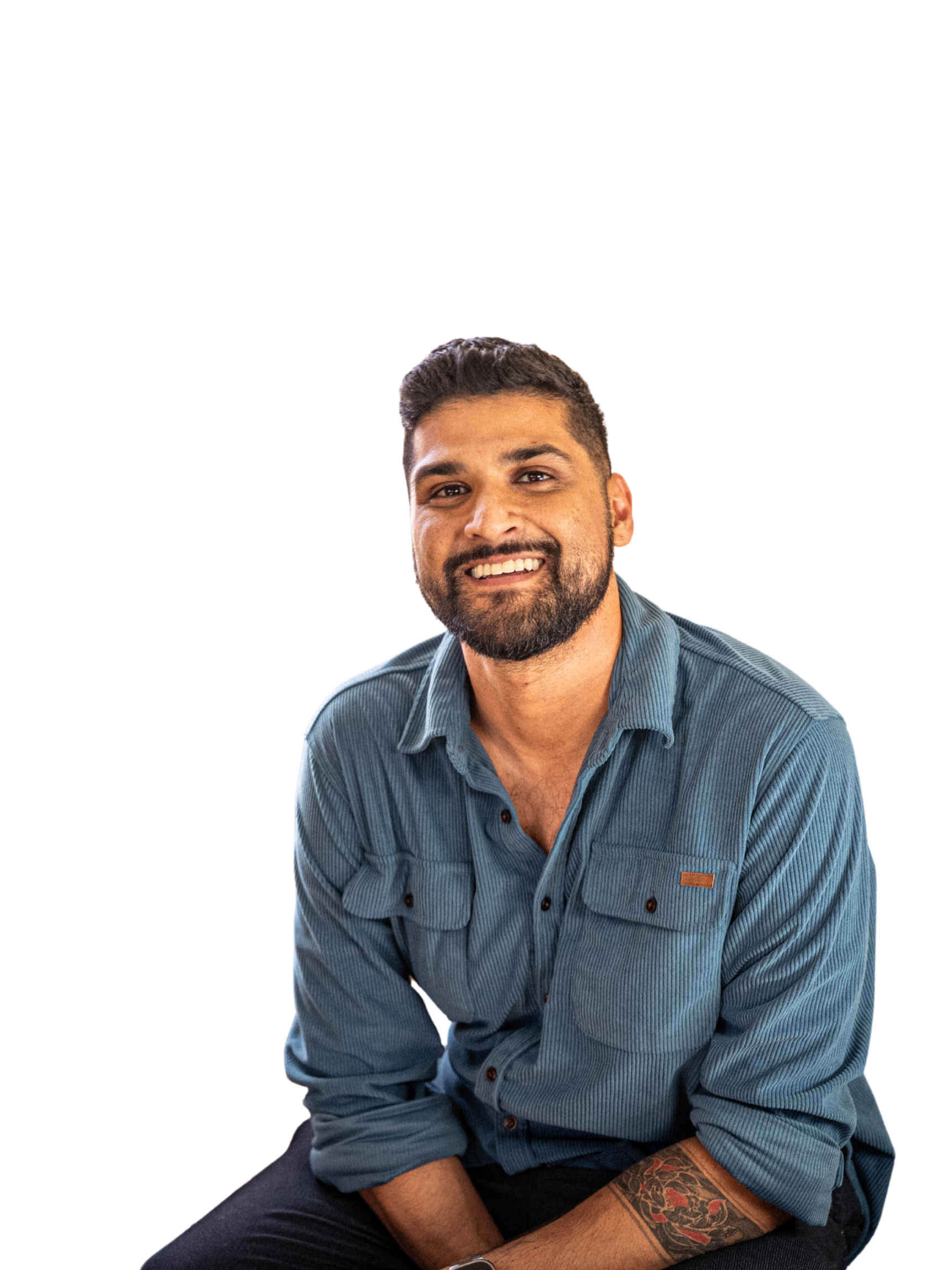 Shaun Alladin LMHC. A smiling man with a dark beard and short dark hair, wearing a blue button-up shirt with rolled-up sleeves, sitting and looking at the camera.
