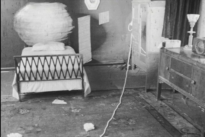 A bedroom with a bed, a wooden dresser, and a paper lantern, arranged with vintage decor and a patterned rug.